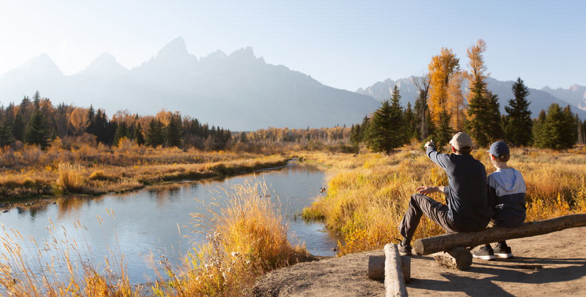 A father and son sit along a river in Grand Teton National Park.