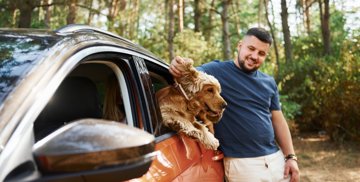 A man stands outside his car and pets his dog in the backseat.