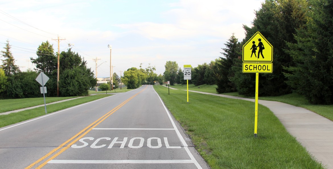 Signs mark a school zone along a suburban road.