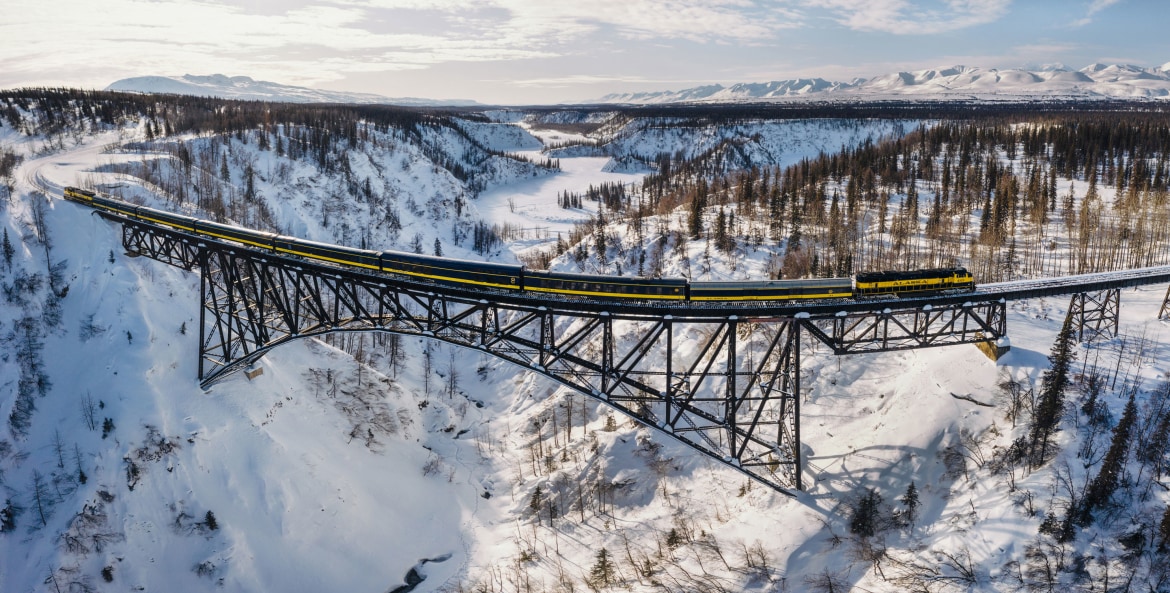 The Aurora Winter Train crosses a bridge over a snow-covered valley in Alaska.