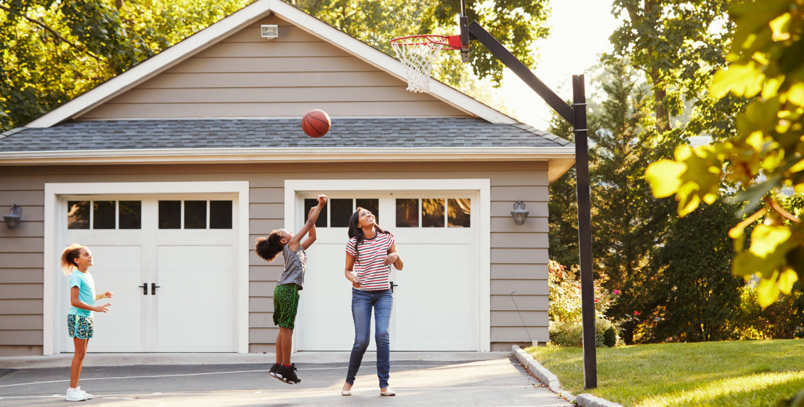 A family plays basketball in their driveway in front of their detached garage.