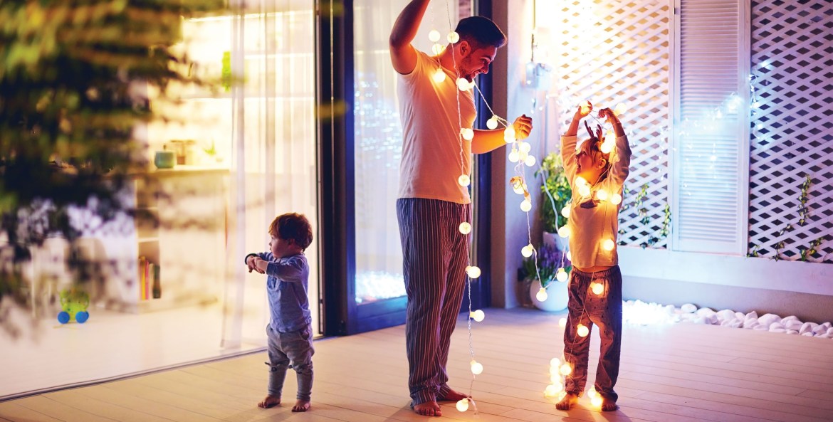 A dad and his two children hang up led string lights on their patio.