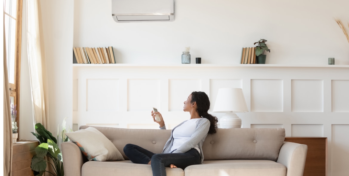 A woman turns on her mini split heat pump while sitting on the couch in the living room.