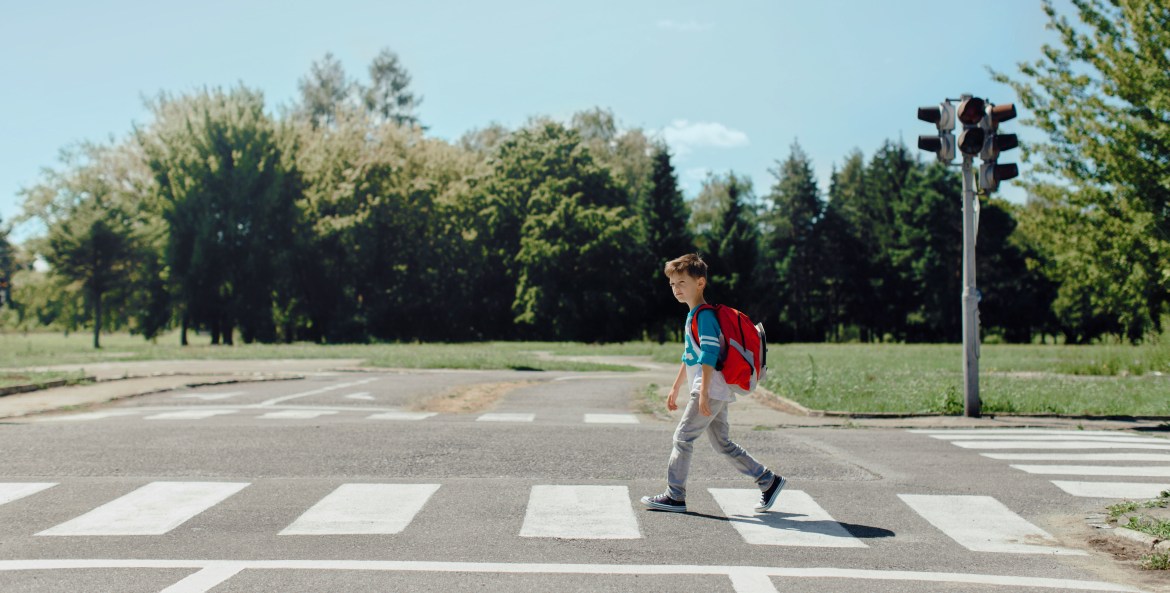 A young boy crosses a crosswalk on a sunny day.