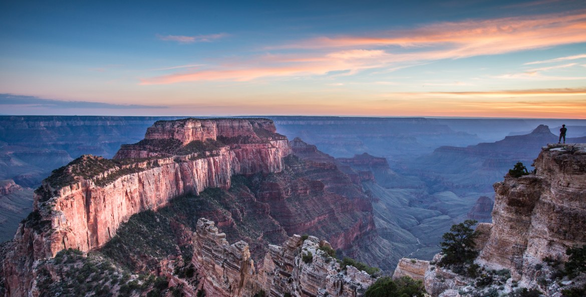 a hiker watches the sunset at the North Rim of the Grand Canyon.