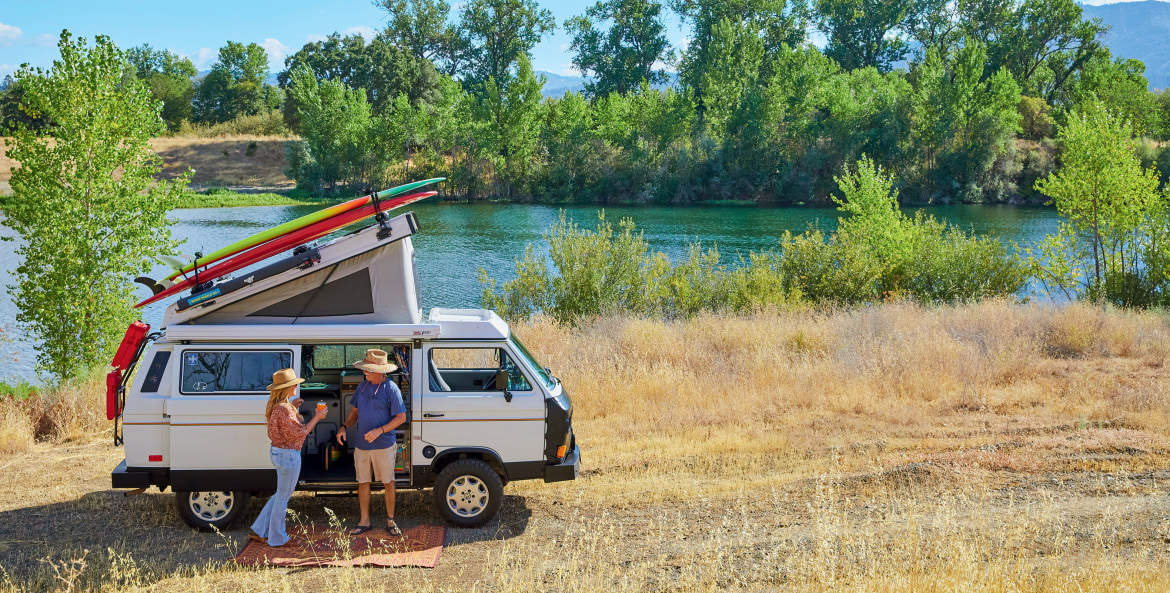 Nanci and Skip Williams outside of their 1987 Volkswagen Vanagon Westfalia along a river in California.