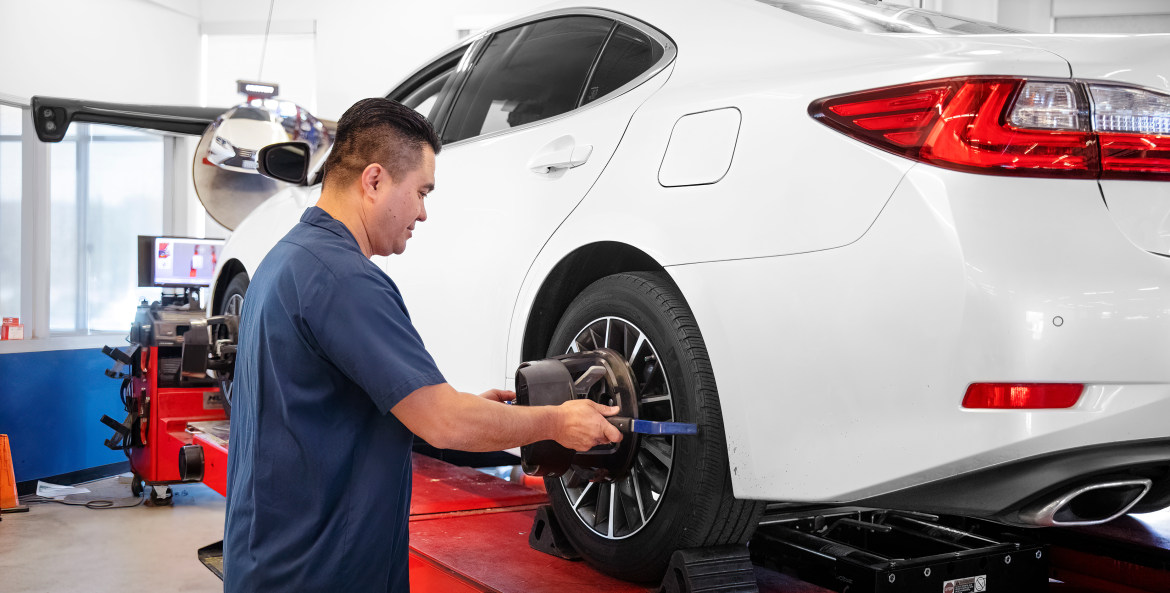 A mechanic inside a AAA Auto Repair Center aligns wheels on a white sedan.