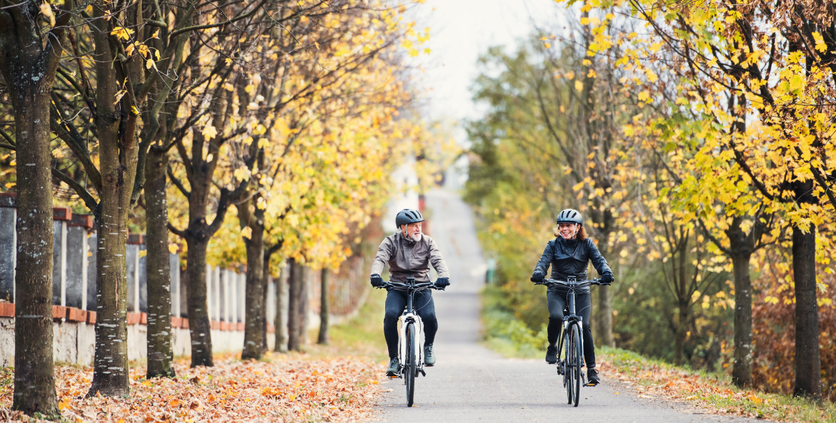 A couple rides their e-bikes on a tree-lined bike path.