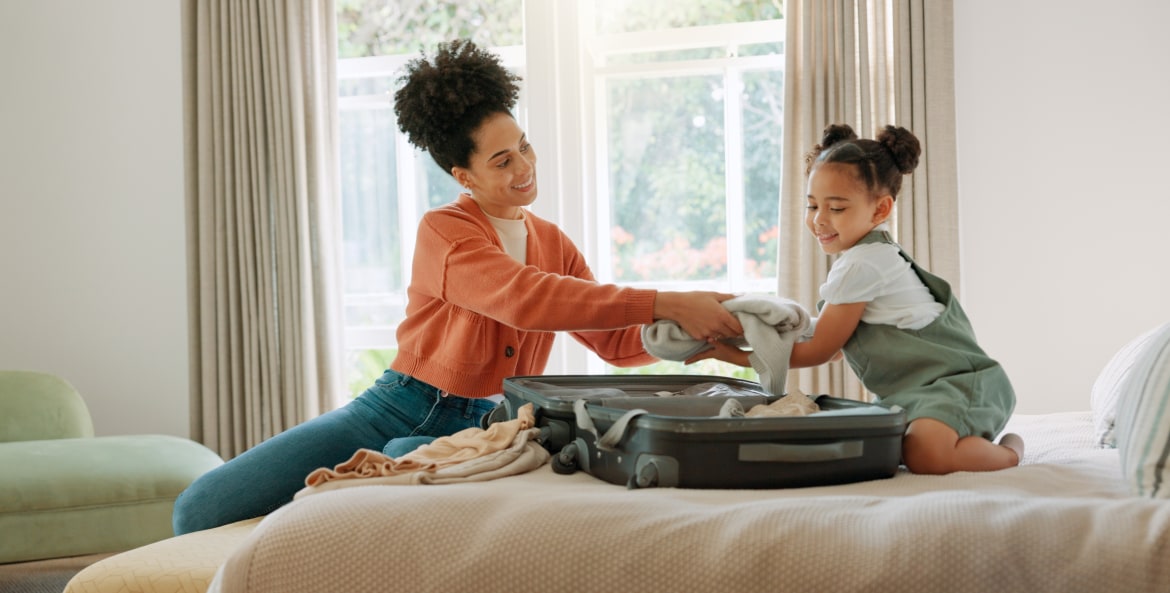 A mother and her daughter pack a suitcase on a bed.