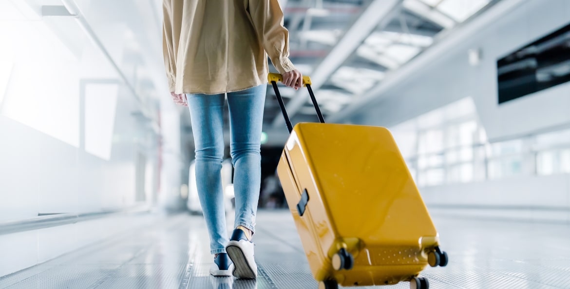 A woman pulls her yellow hard-sided suitcase through the airport.