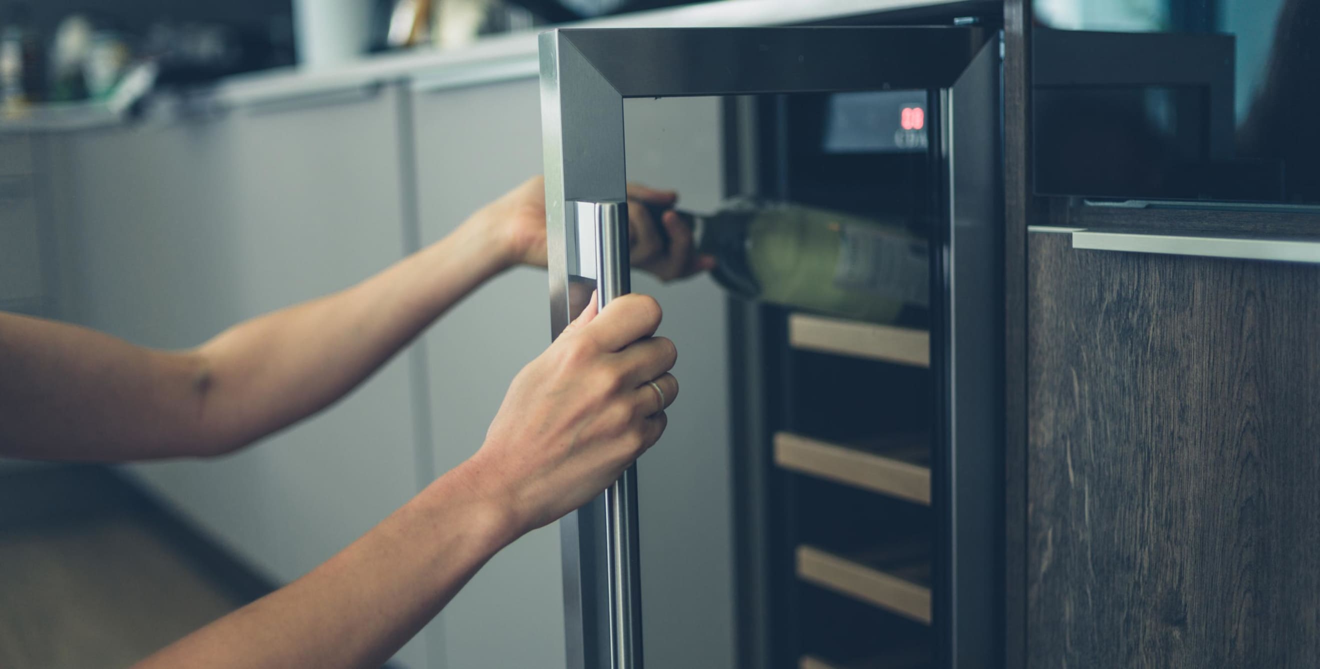 A woman's arm reaches into a wine fridge to remove a bottle of white wine, picture