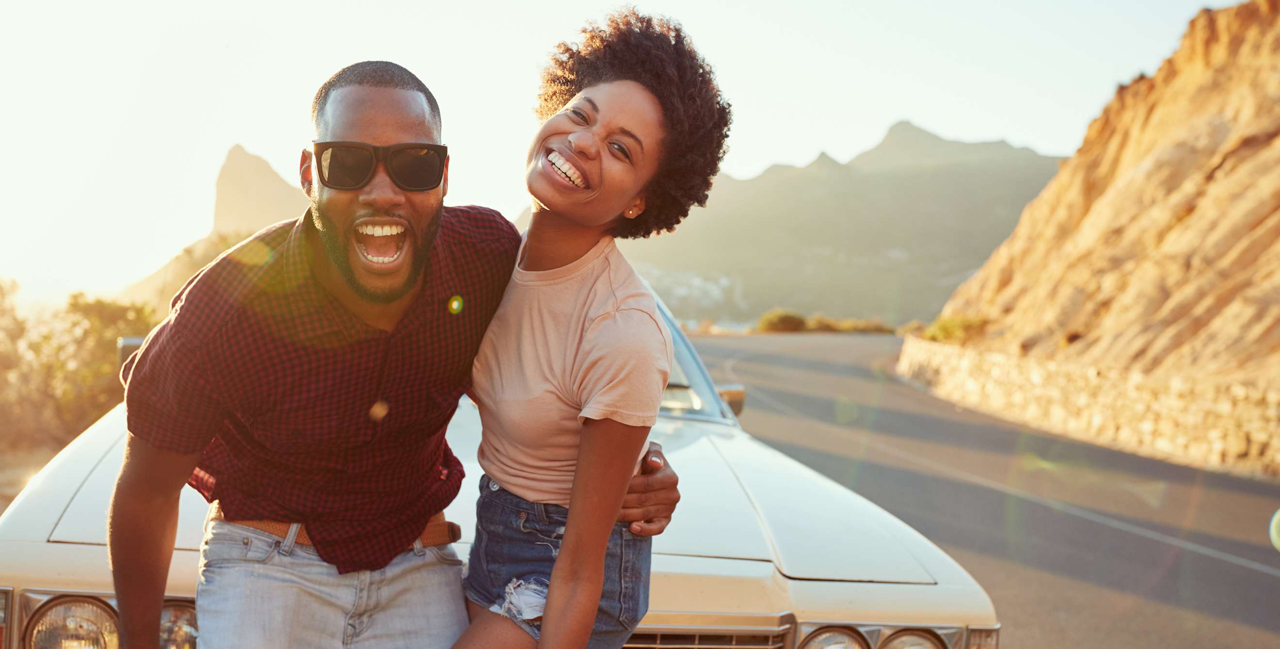 African American couple stand in front of a classic car along the bluffs at sunset