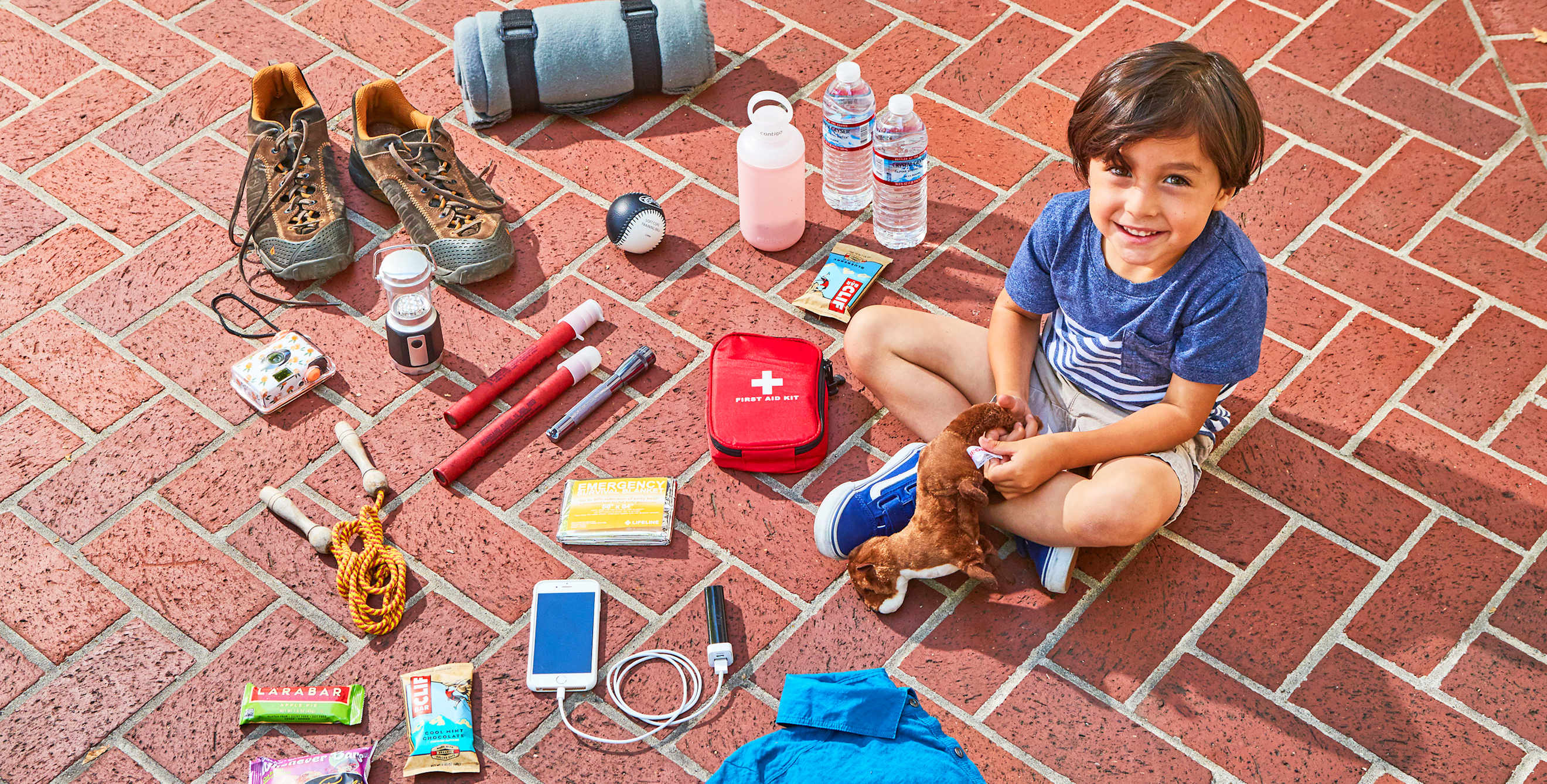 boy seated on ground with an array of emergency road kit essentials