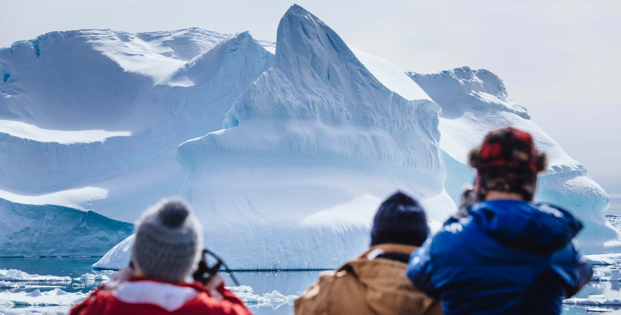 three people wearing coats and caps view glacier from boat, picture