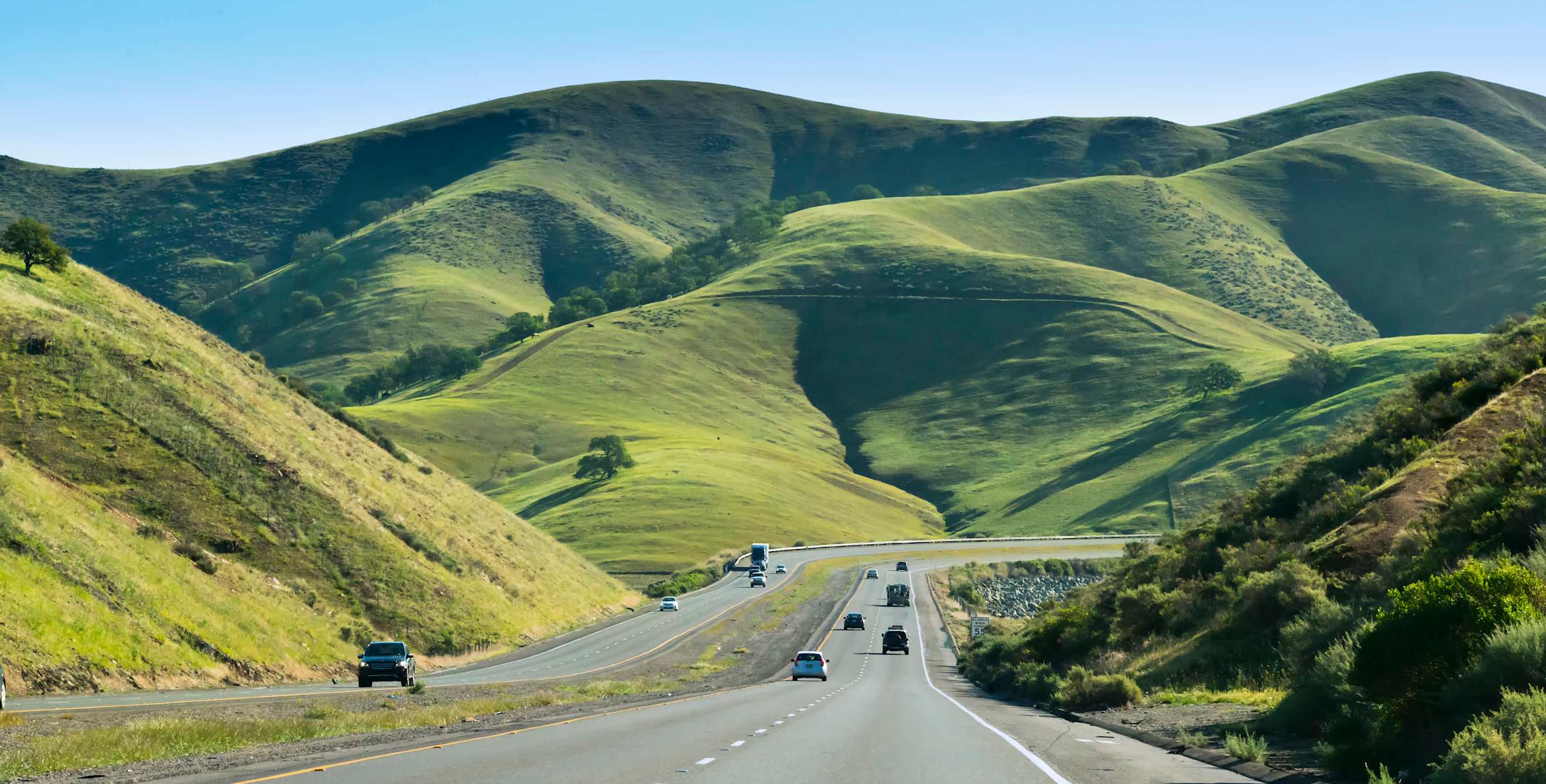 autos on divided highway with green hills in background