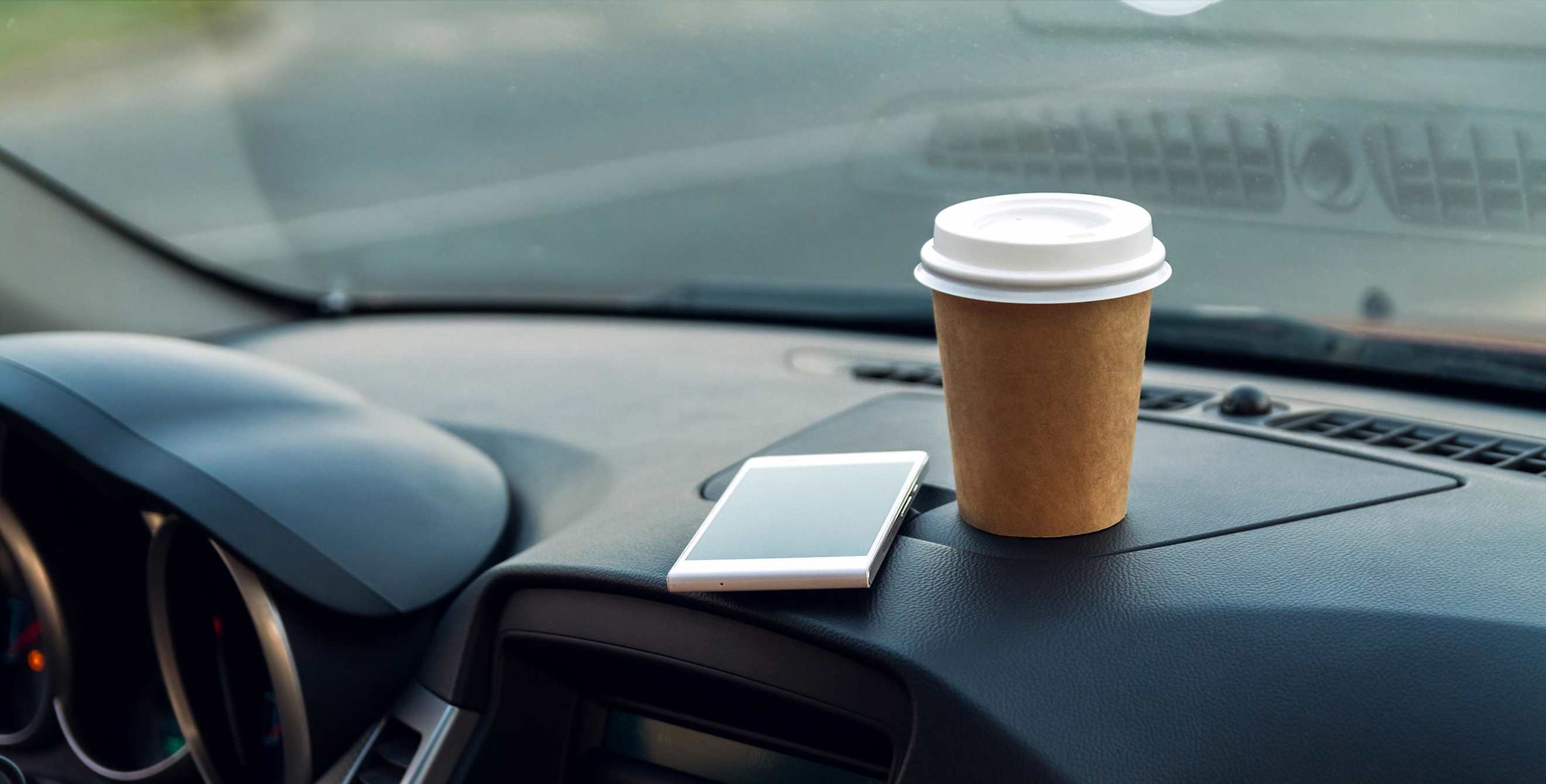 car dashboard with a cell phone and cup of coffee.