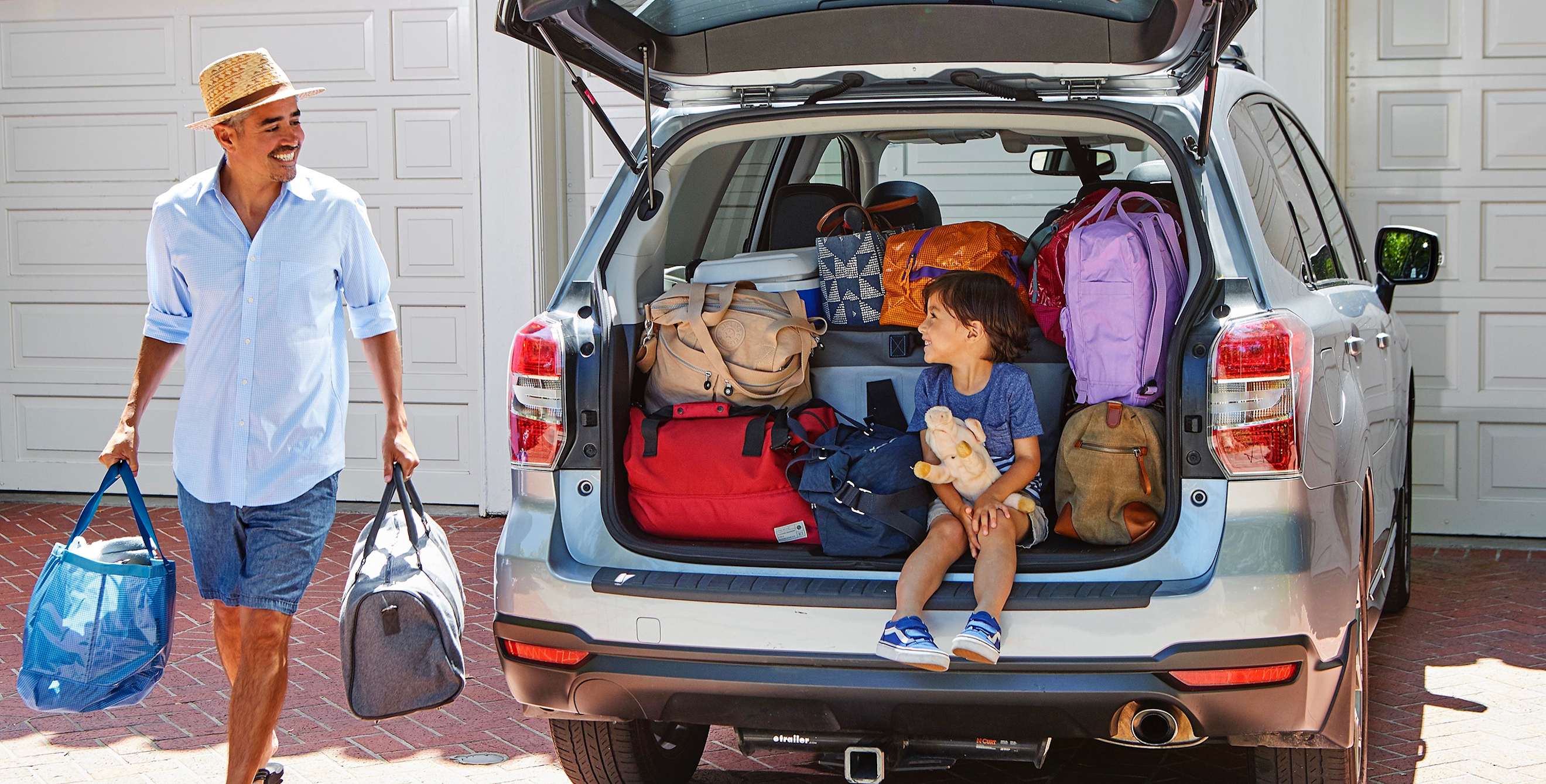 man carries soft tote bags to load into car hatchback while boy watches, picture