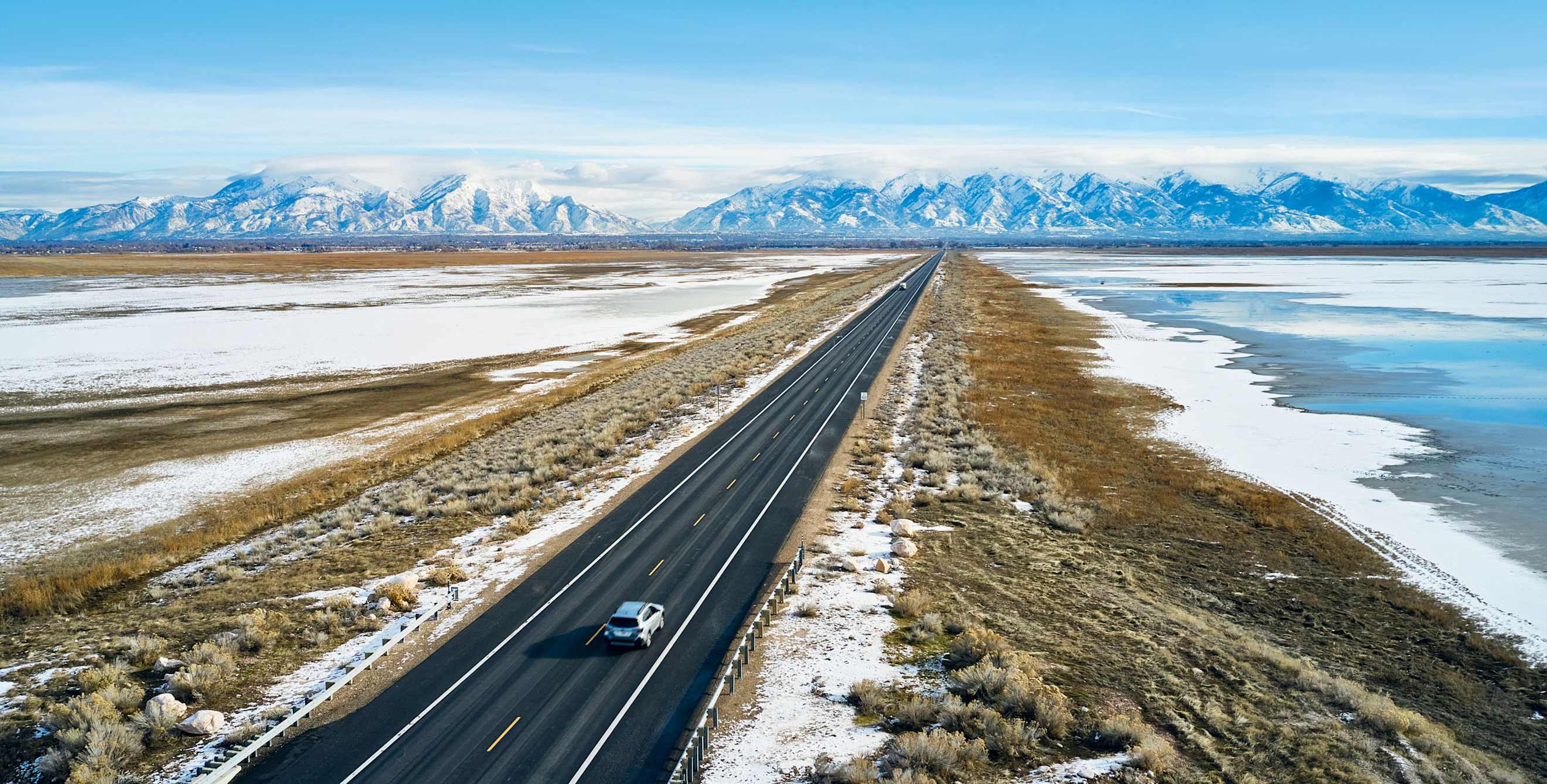 Cars drive on a road surrounded by a dusting of snow.