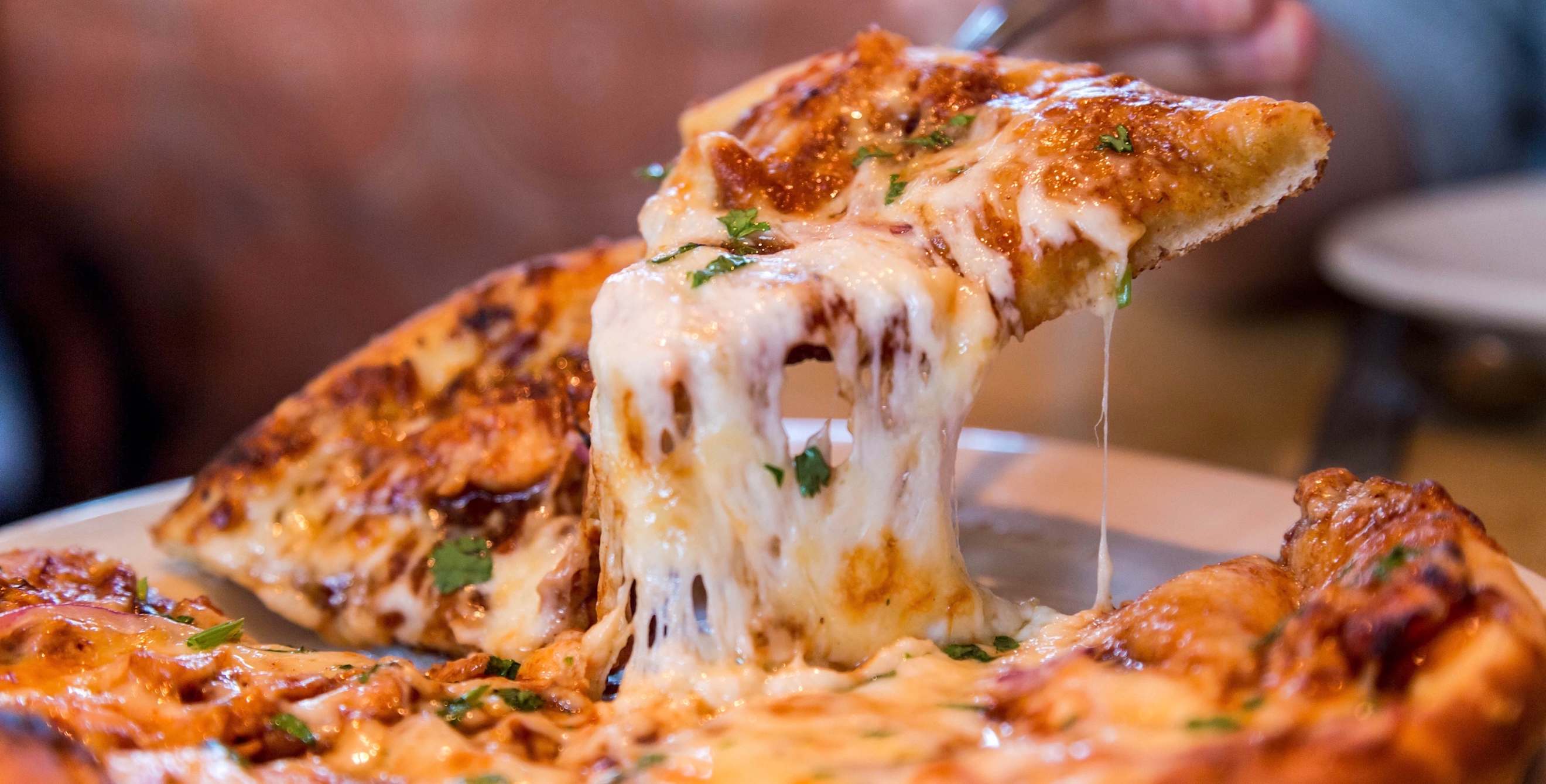 picture of a slice of cheesy pizza being lifted from the whole pie