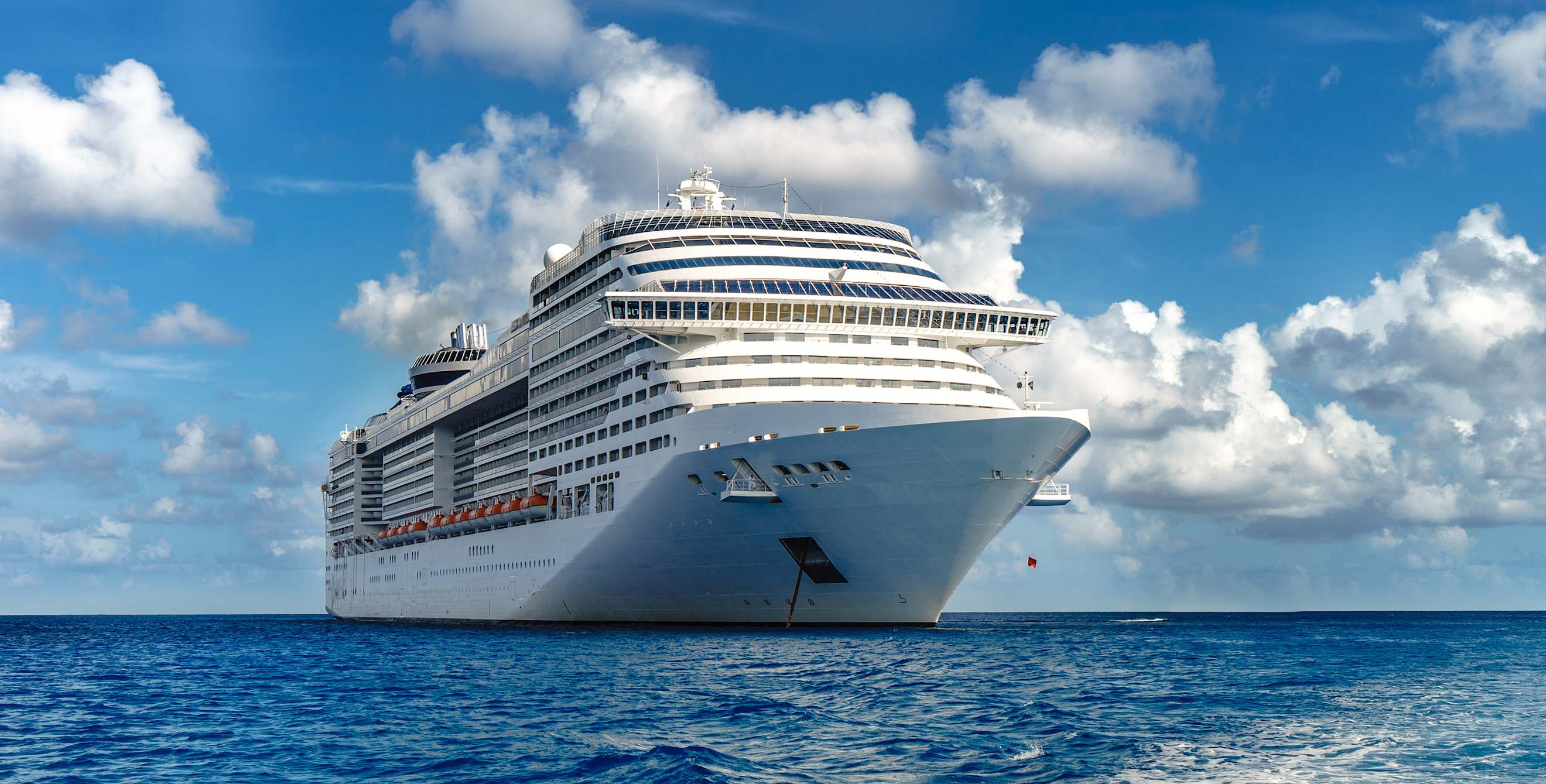 a cruise ship on the open ocean with a blue sky and clouds in the background