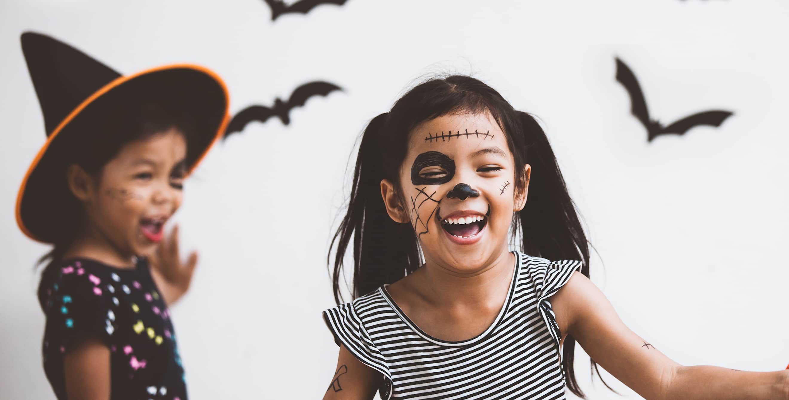 Two girls with face paint put up Halloween decorations bats