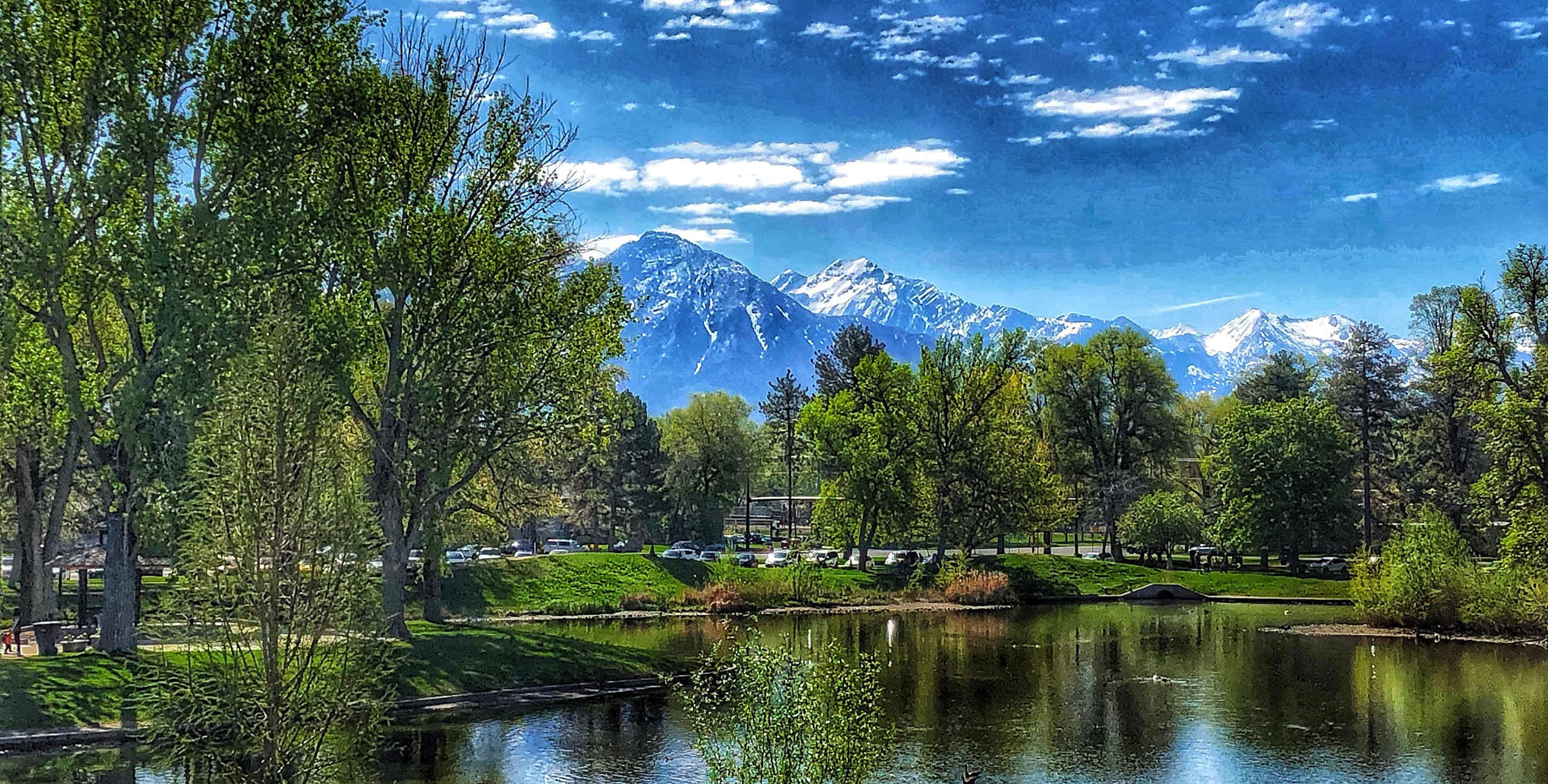 Liberty Lake surrounded by green, leafy trees under blue, partly cloudy sky at Liberty Park in Salt Lake City, Utah, picture
