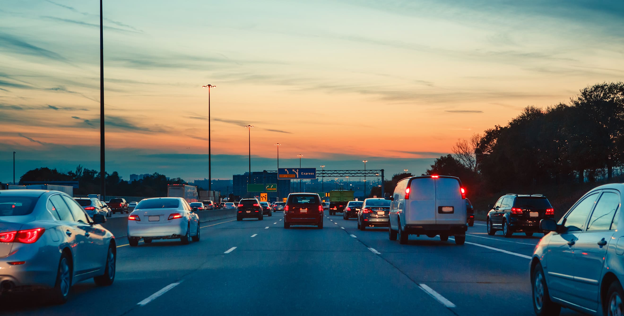 Cars on the freeway at night with an orange sunset in the background.