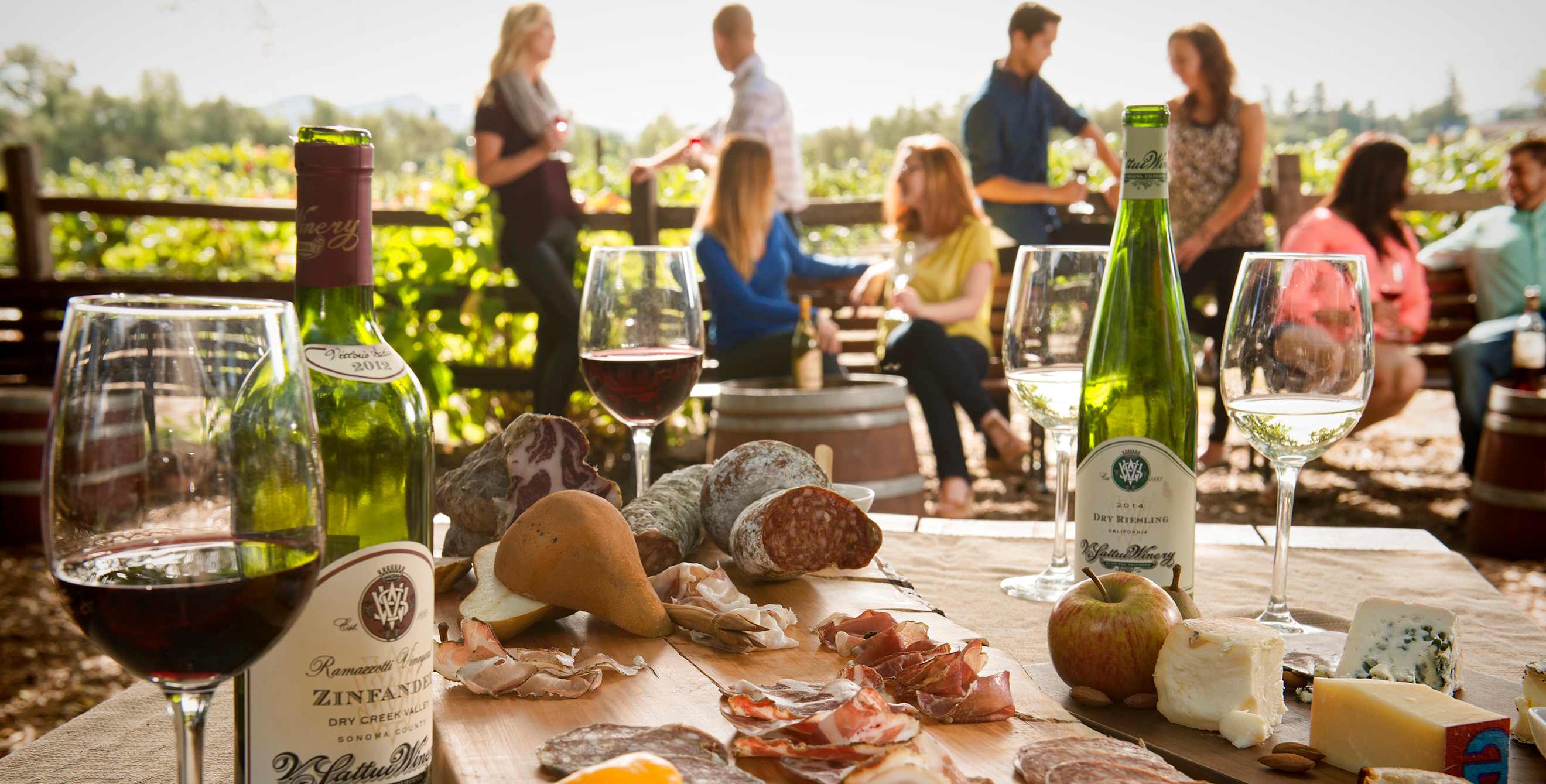Picnic spread of wine, cheese, and meats set amid visitors at a California winery