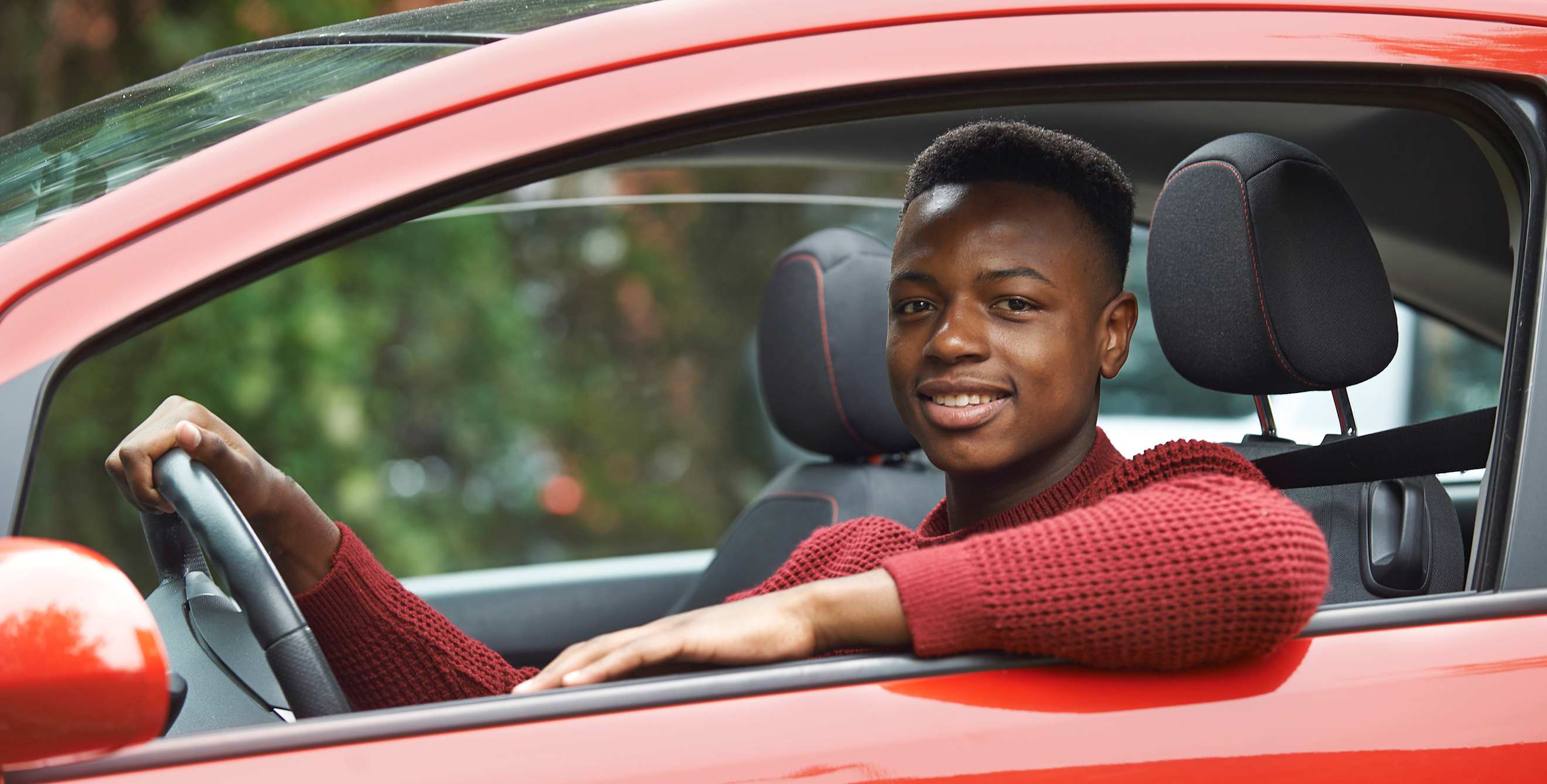 Teen in the drivers seat of a red car.