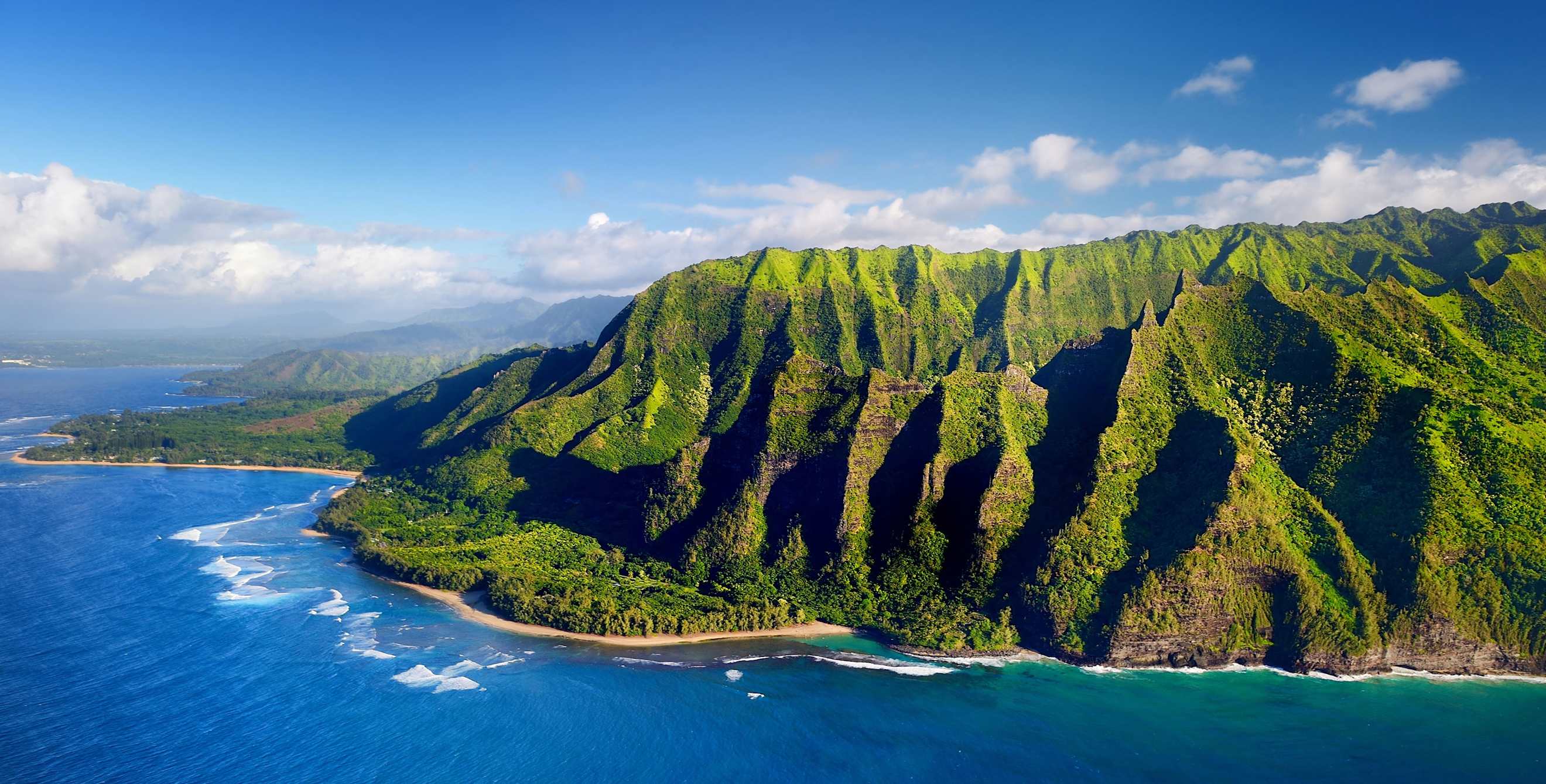 aerial view of surf breaking against rocky and lush Nāpali Coast on Kauai, Hawaii