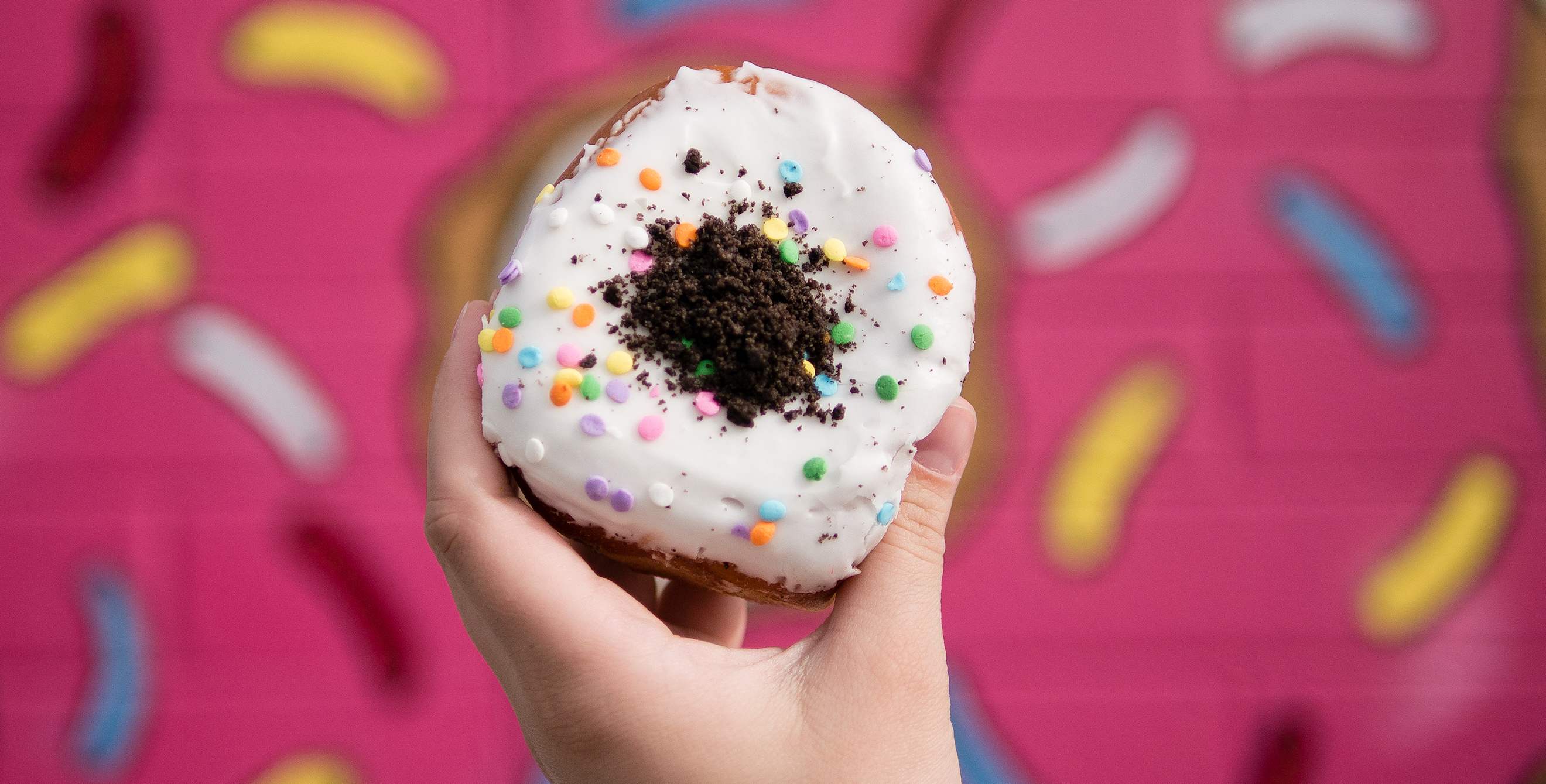 A hand holds a Oh My Birthday Cake Oreo stuffed donut from the Las Vegas Donut Bar, image