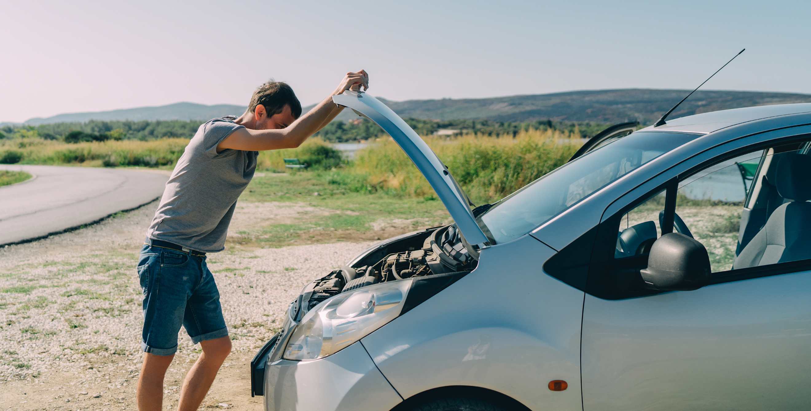 man by side of road with car hood up