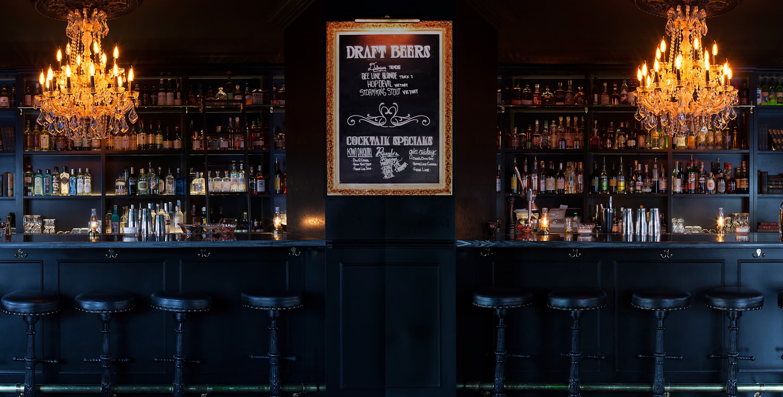 Two chandeliers hang over Death and Taxes ornate black bar, image