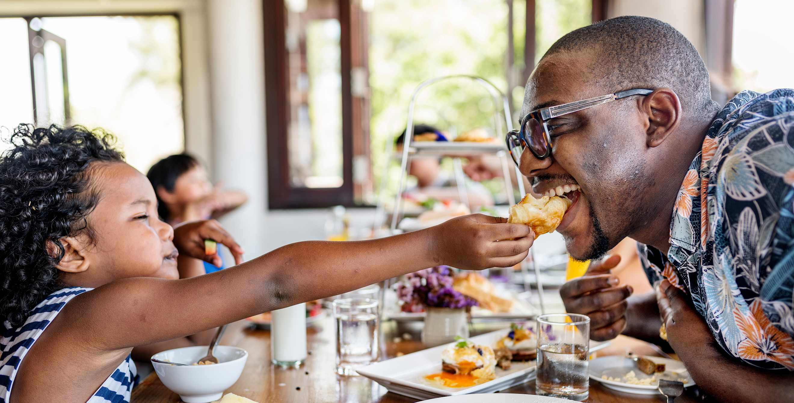 A dad eats a bite of breakfast from his son's hand, image