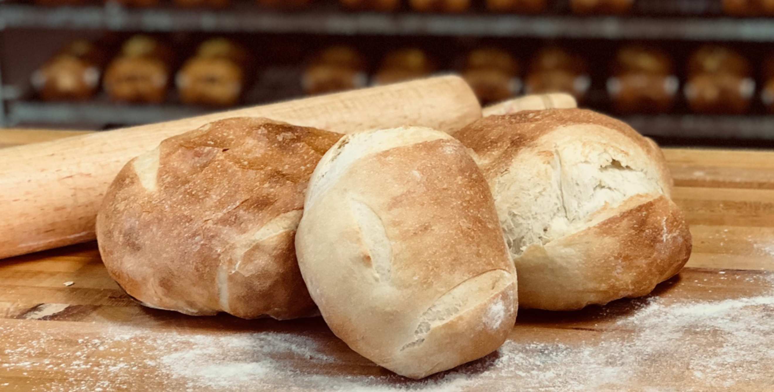 picture of three loaves of sourdough bread on a flour-covered wood blog at Honey and Grains bakery