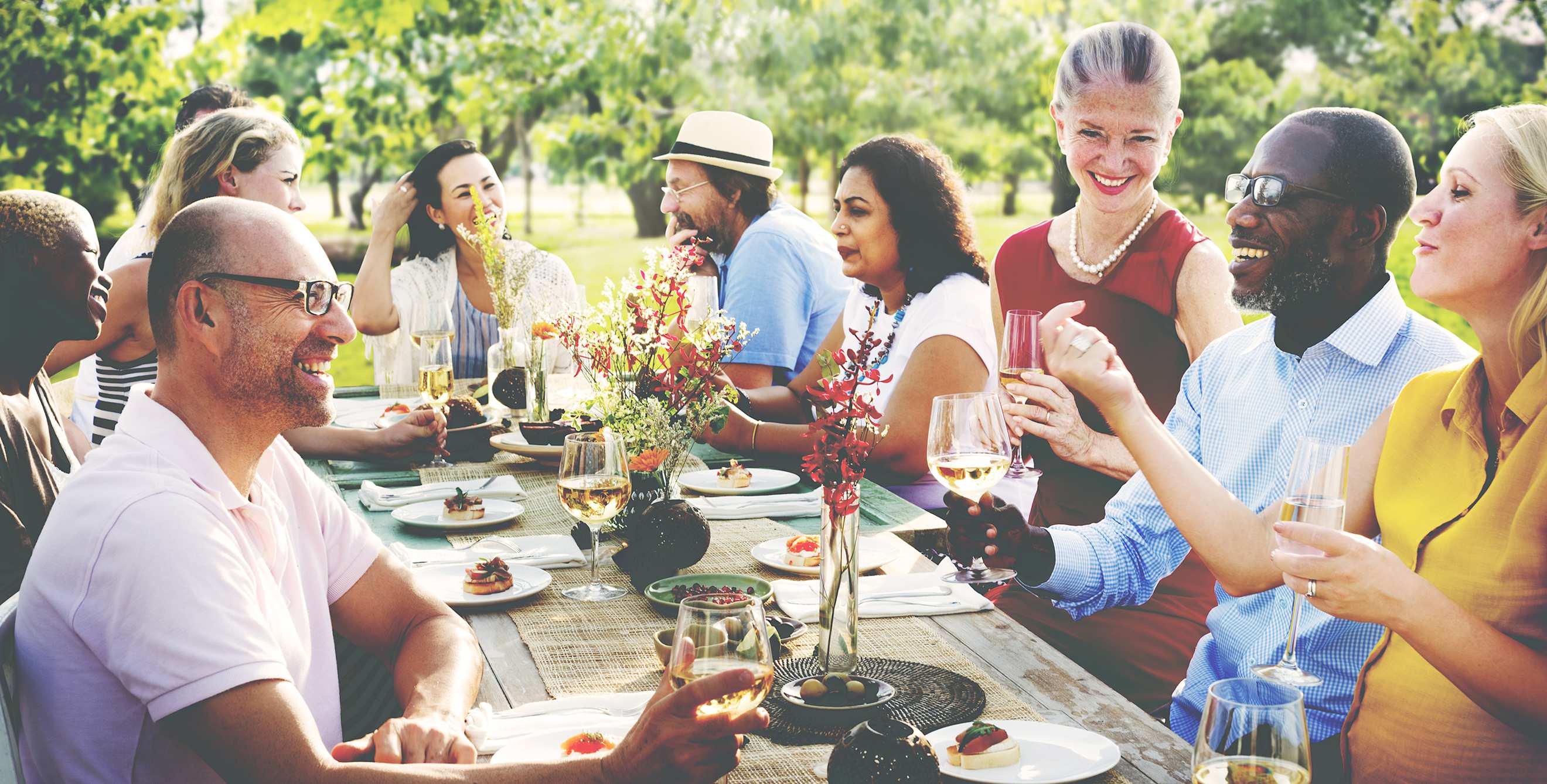 Family eating and chatting around a large outdoor table, image