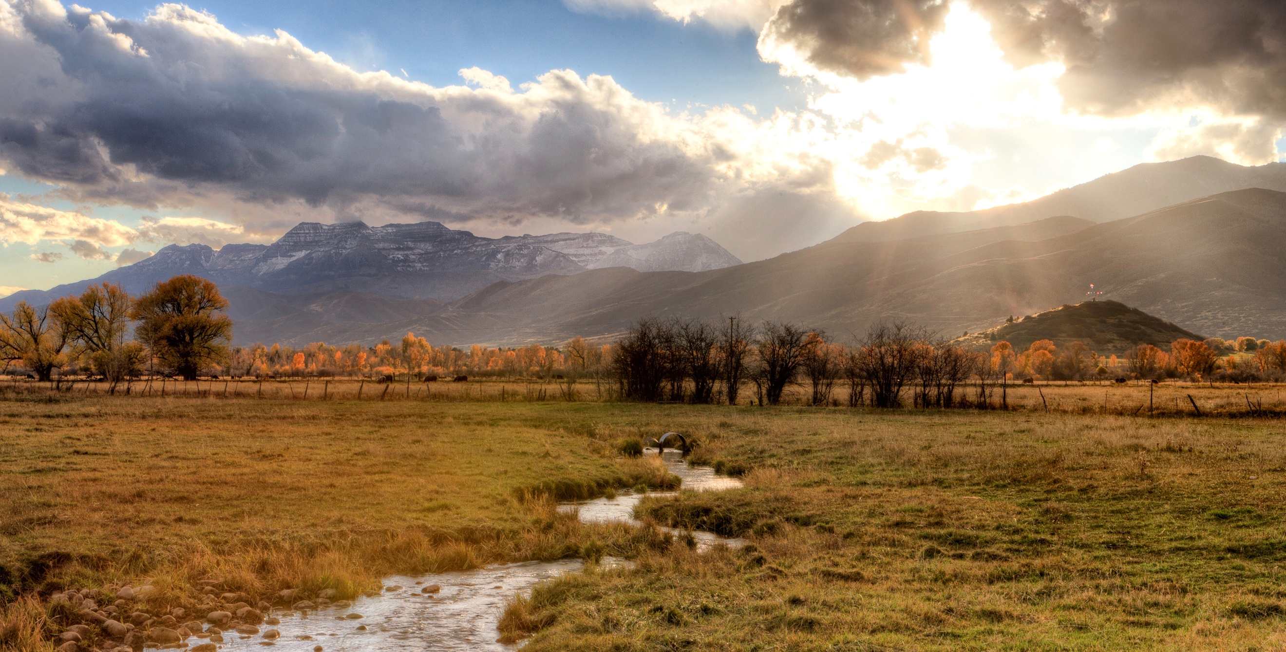 a stream passes trough a lush meadow with the sun poking through rain clouds in Heber Valley, Utah