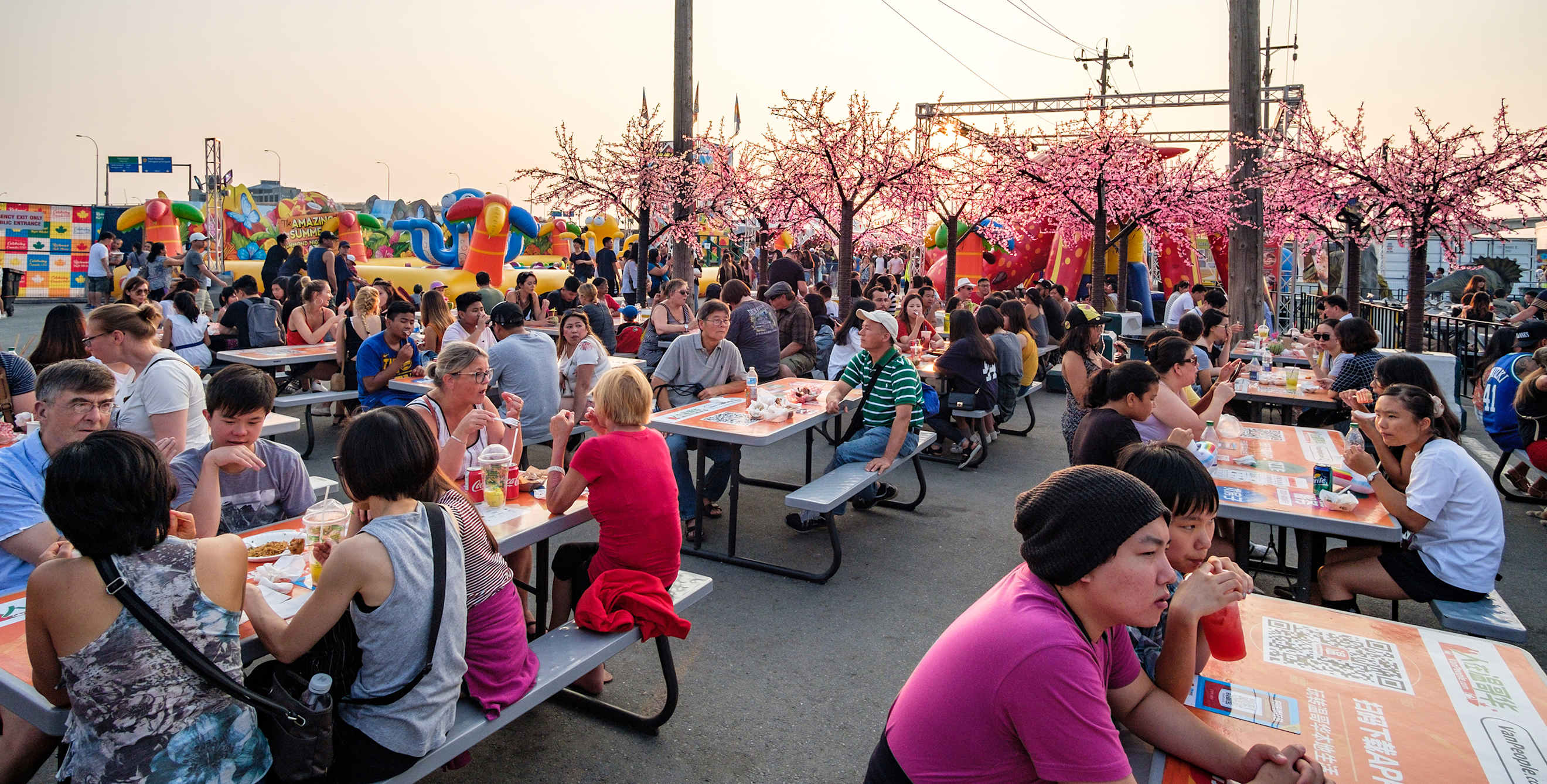 People eat at picnic tables at the Richmond Night Market at dusk, image