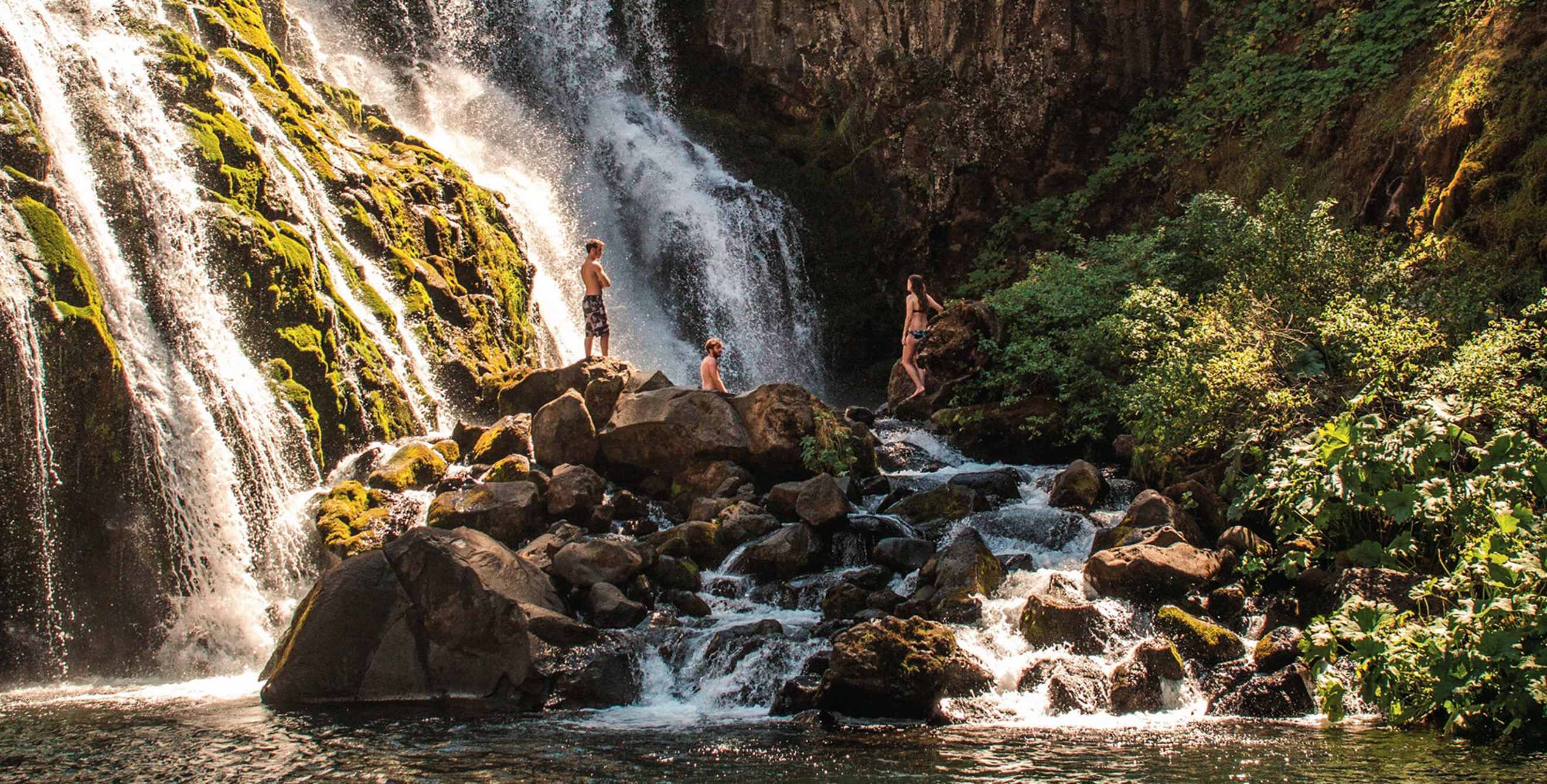 trio of swimmers admire Middle Falls from rocks below on the McCloud River near Mt Shasta, California