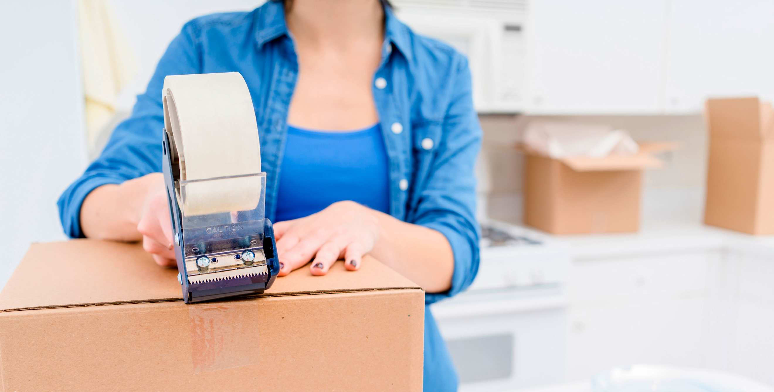 picture of a woman applying packing tape to a cardboard box