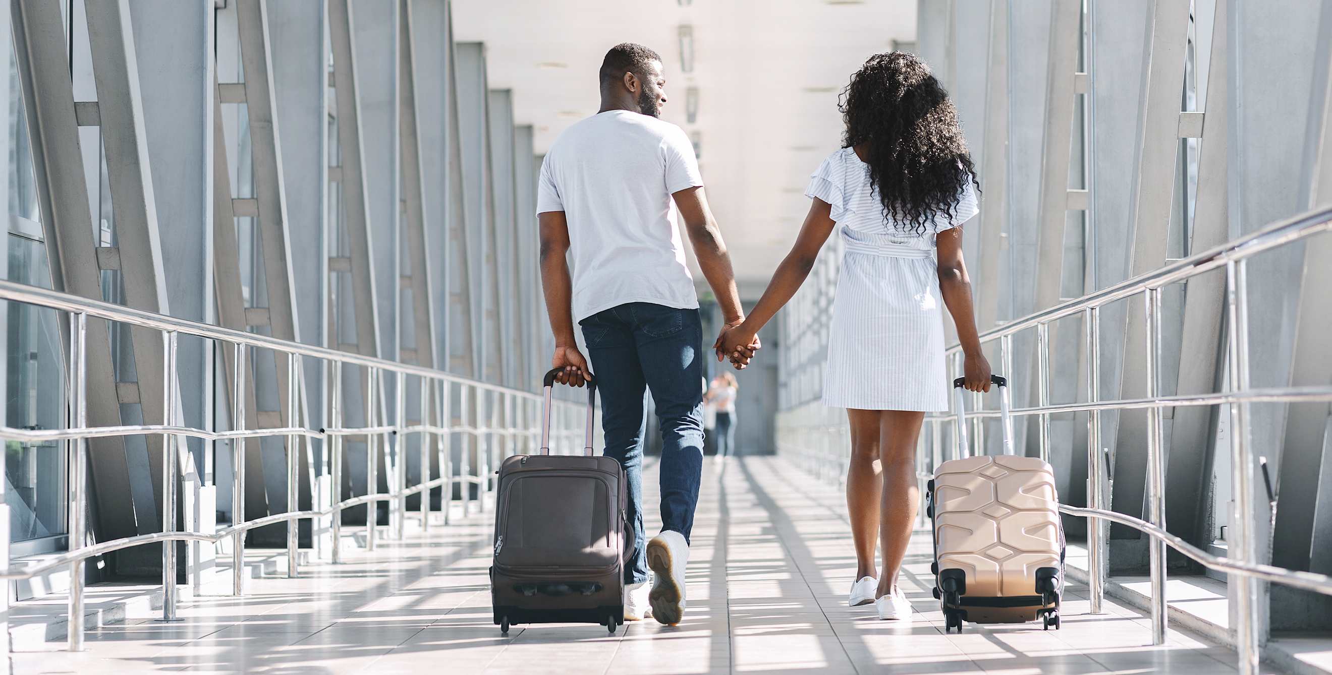 A couple walk down a airport hallway with rolling bags.