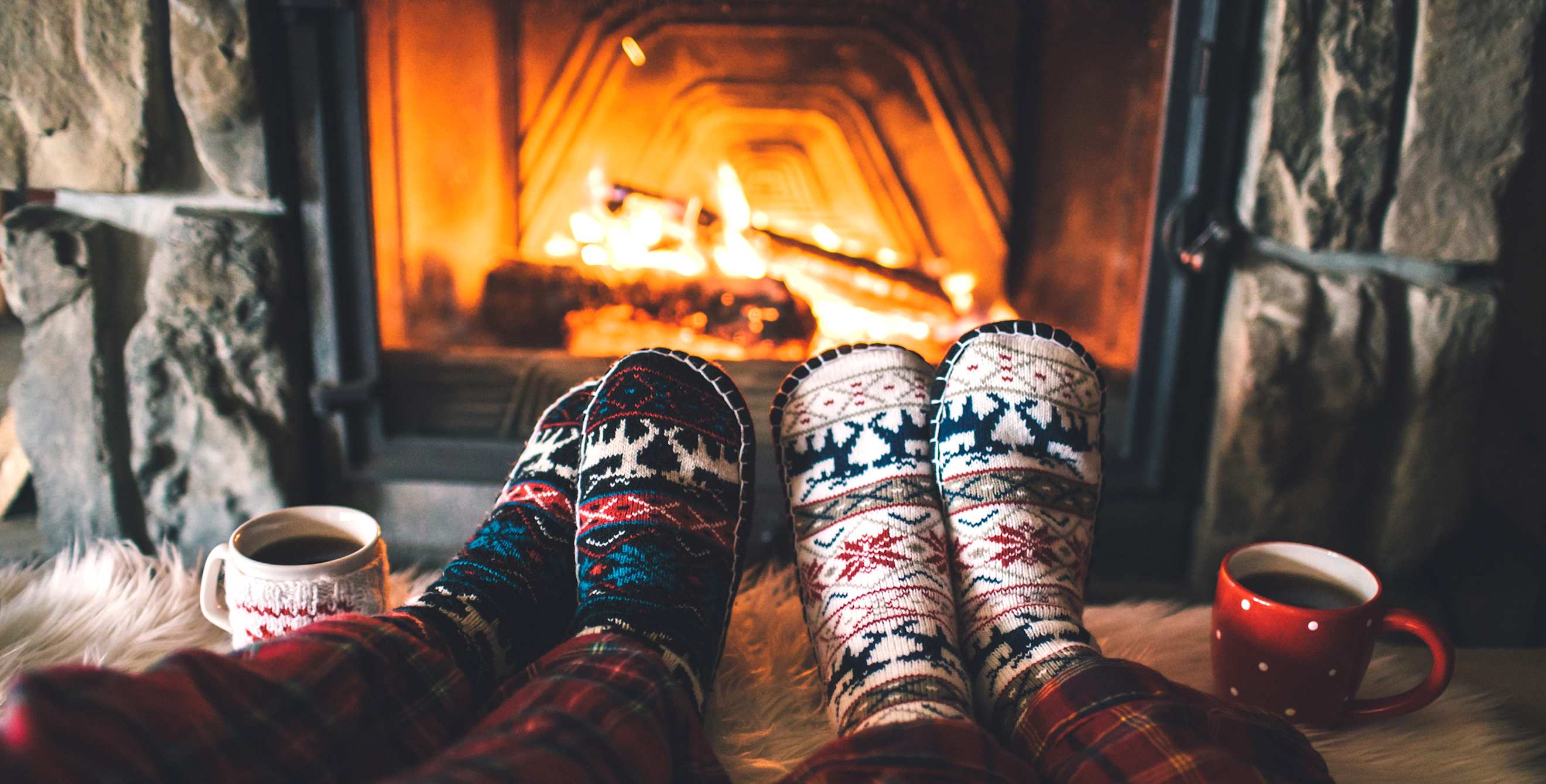 A couple warm their feet in front of a fire.