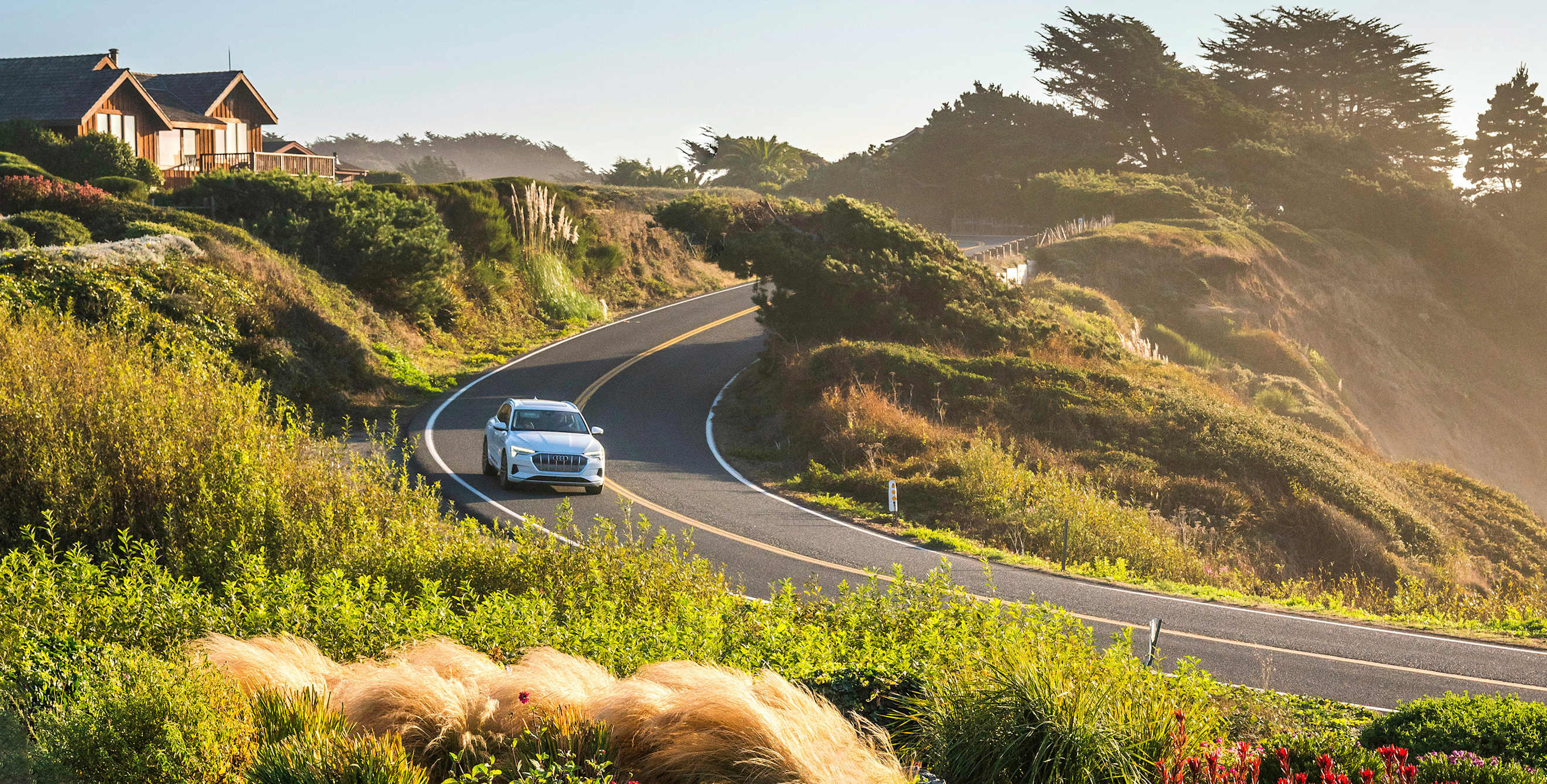 An Audi E-Tron sedan navigates a curve along the coast on a sunny afternoon near Mendocino, California