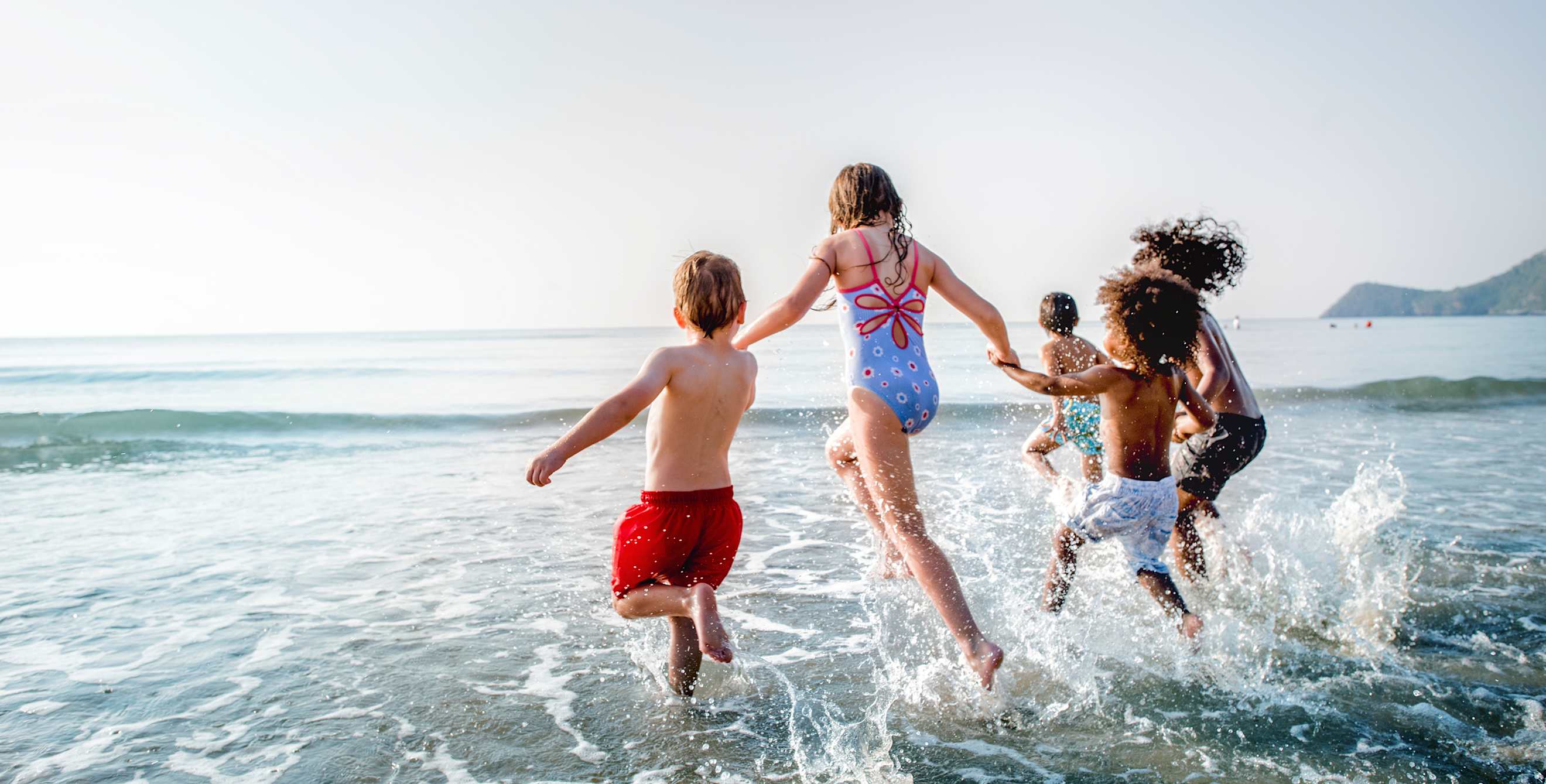 kids holding hands and running into the waves together.