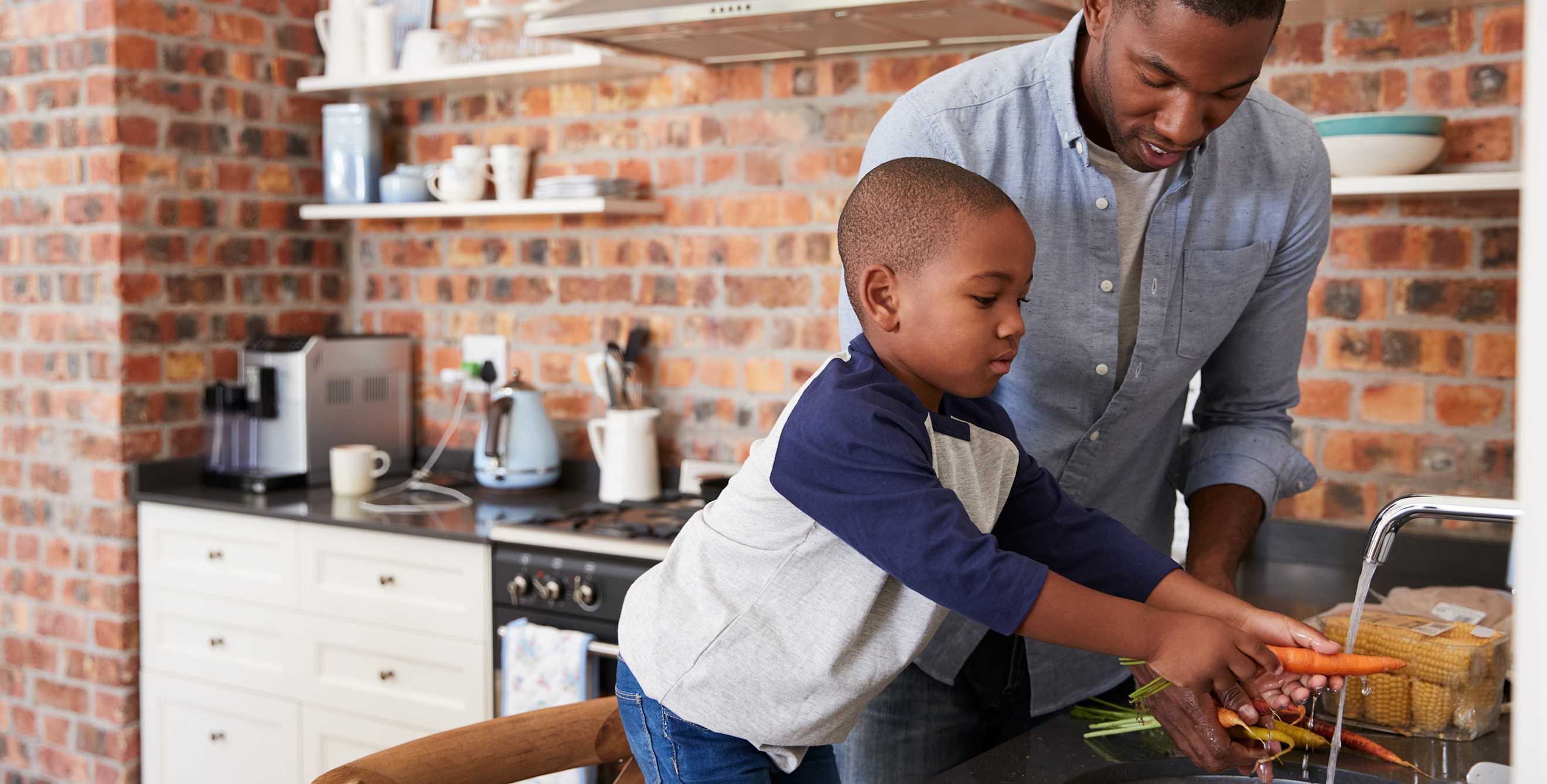 A young son and his dad wash carrots before cooking together.