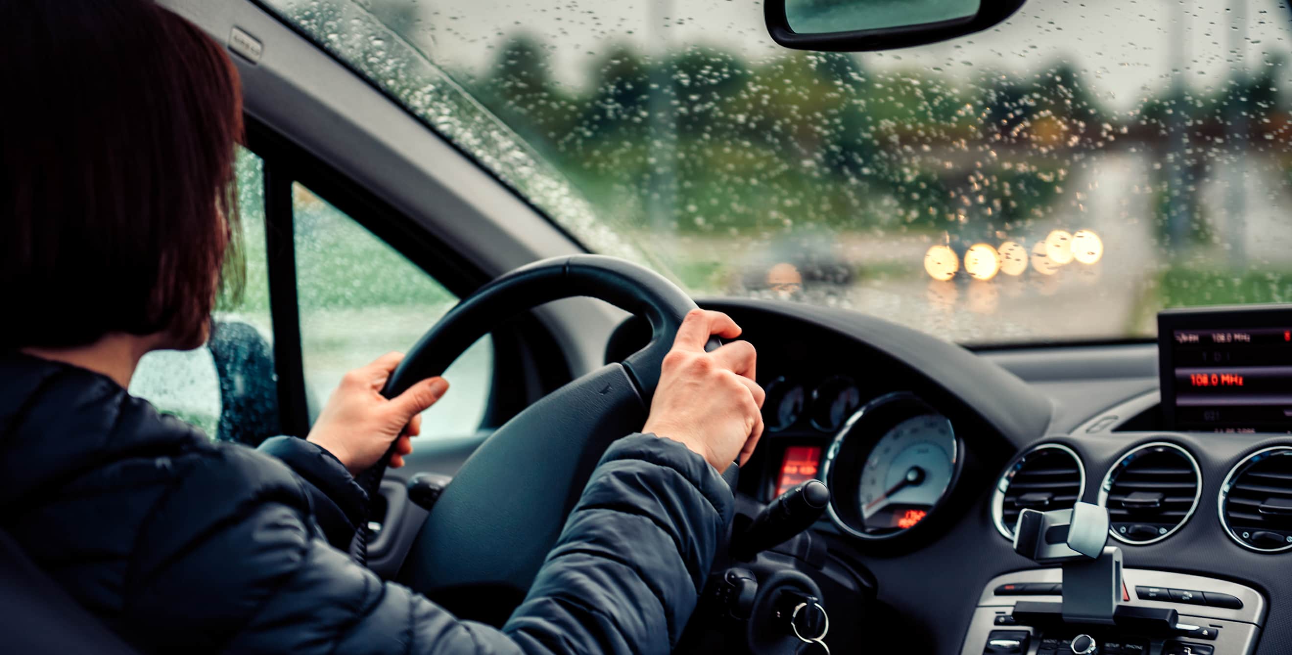 A woman grips the steering wheel with two hands while driving in the rain.
