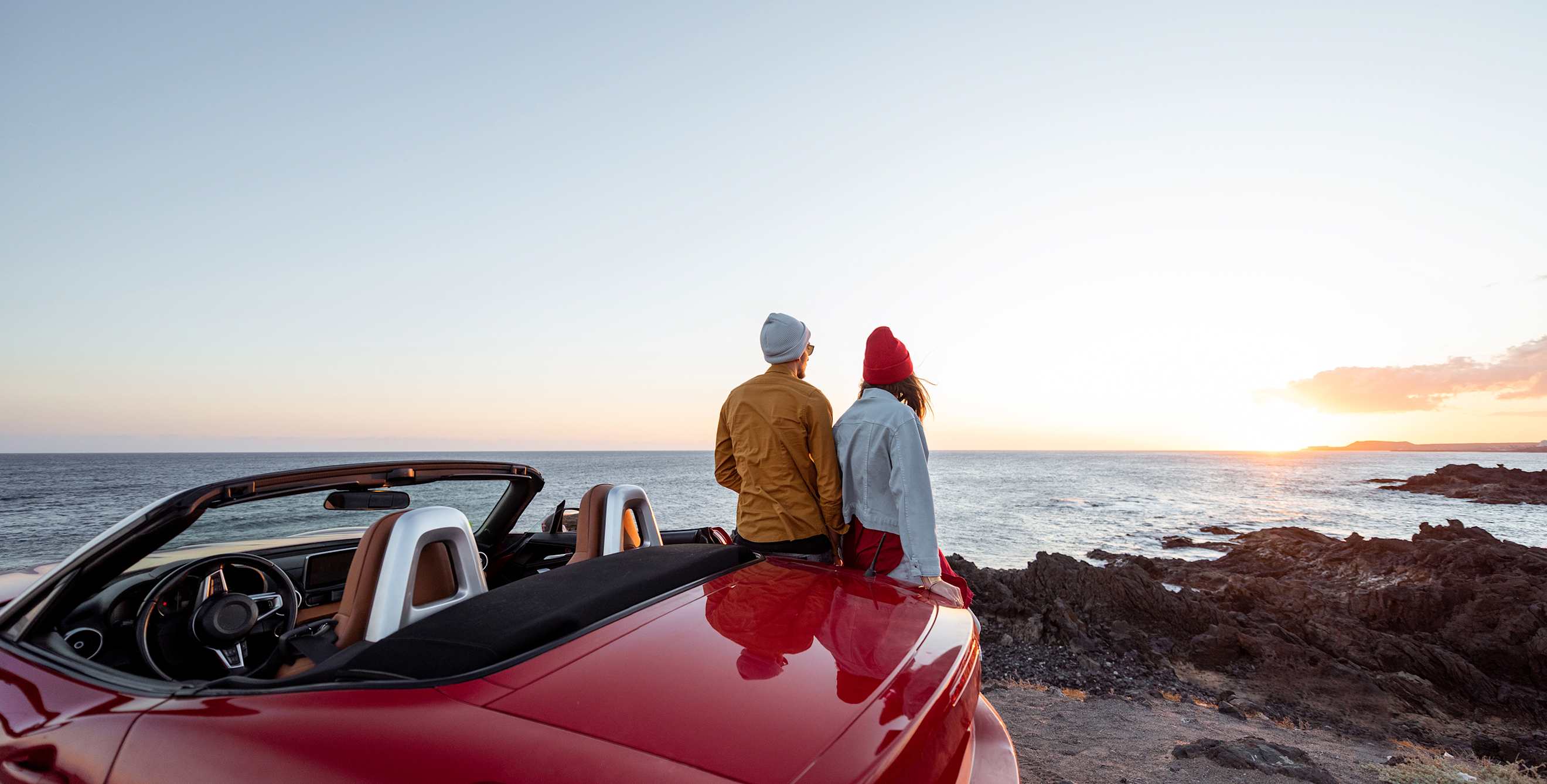 A couple watch the sunset over the ocean from a roadside overlook.