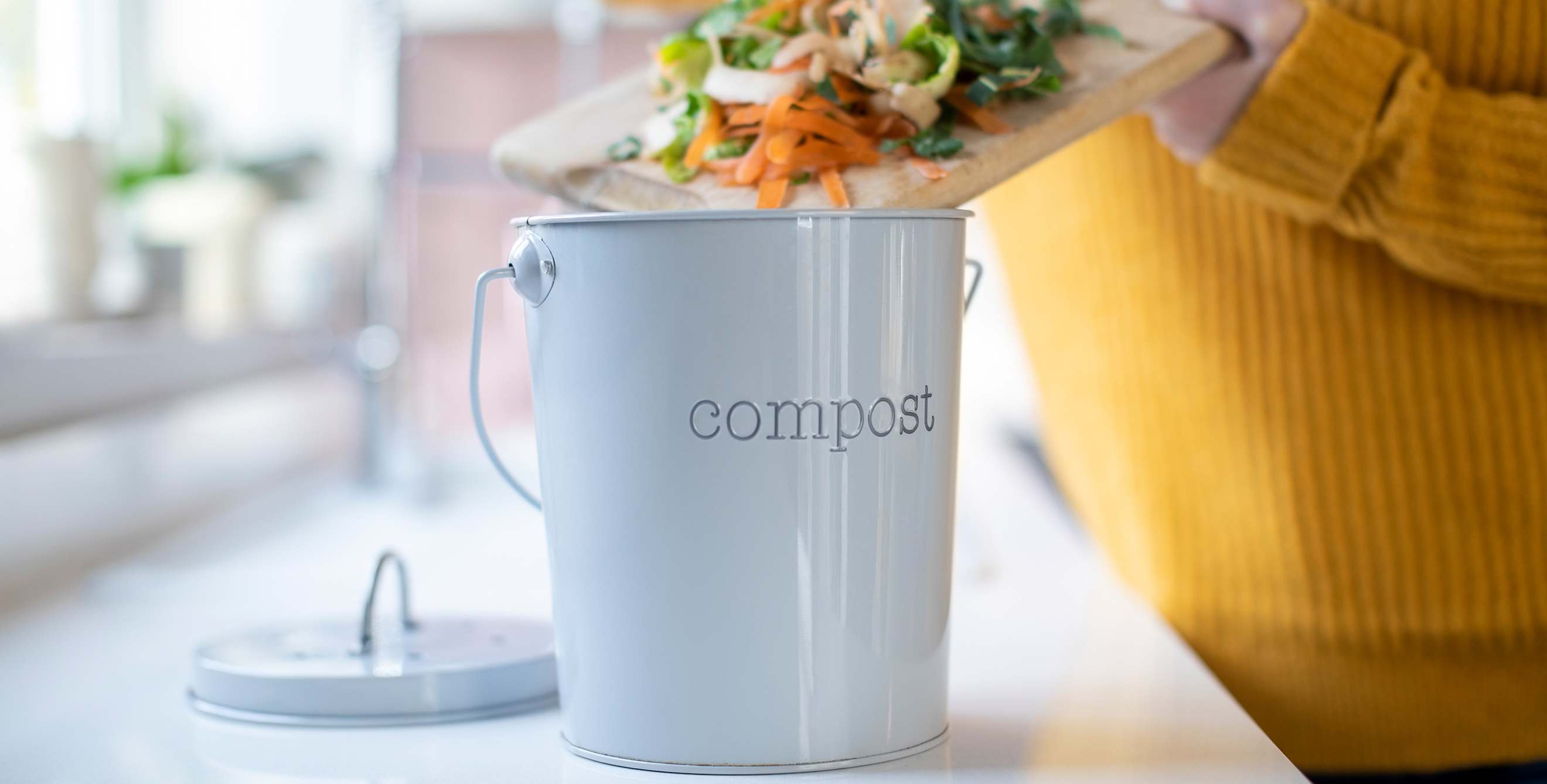 A woman puts scraps into her countertop compost bin.