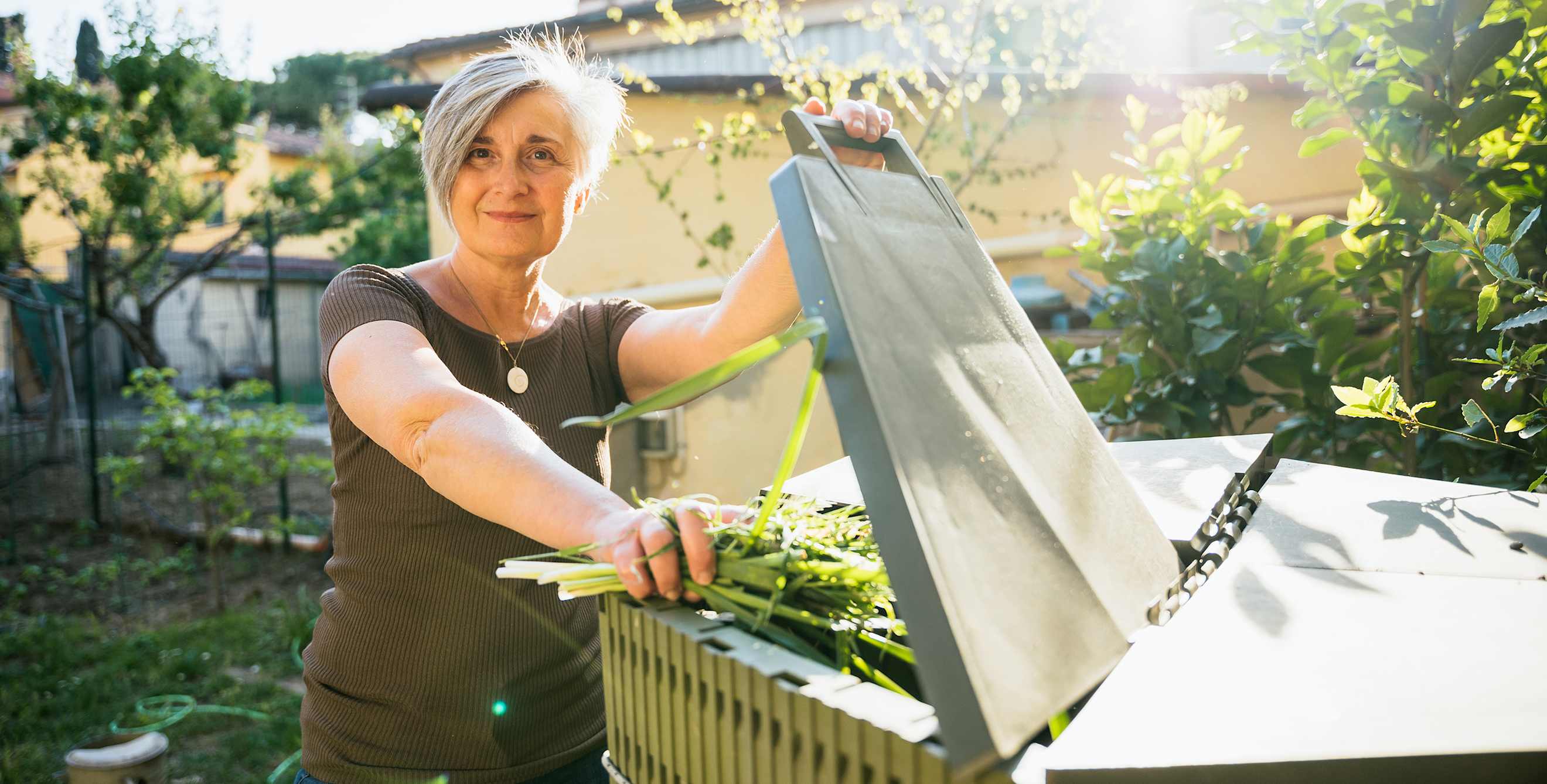 A woman puts greens into her backyard compost bin.