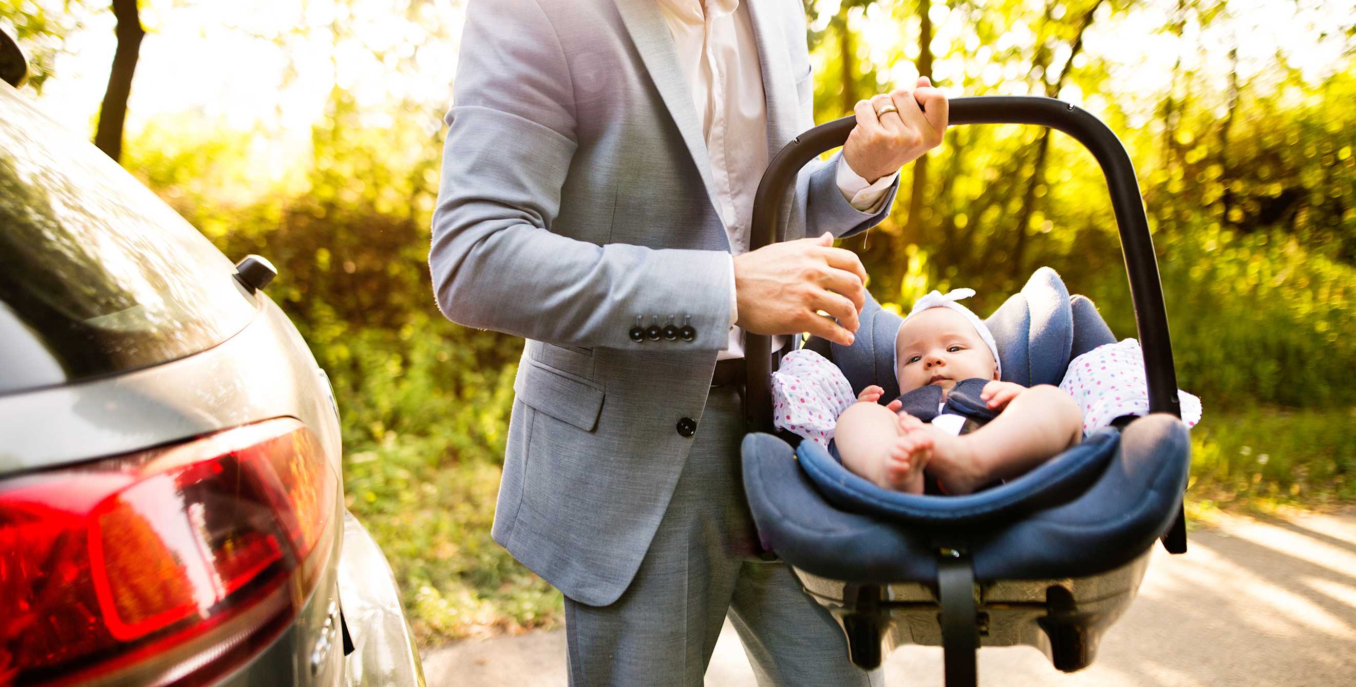A father carries an infant in a car seat.